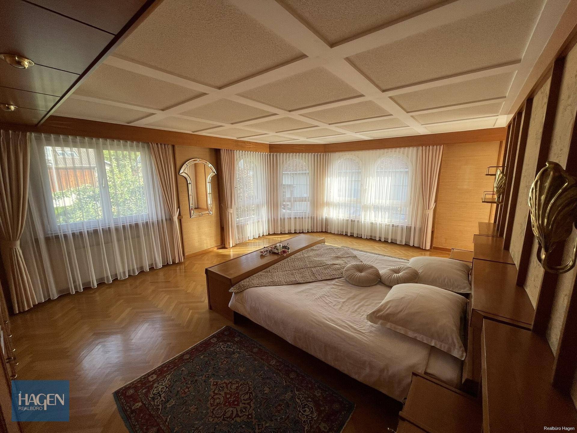 Großes Schlafzimmer mit Parkettboden, Kassettendecke und vielen Fenstern.