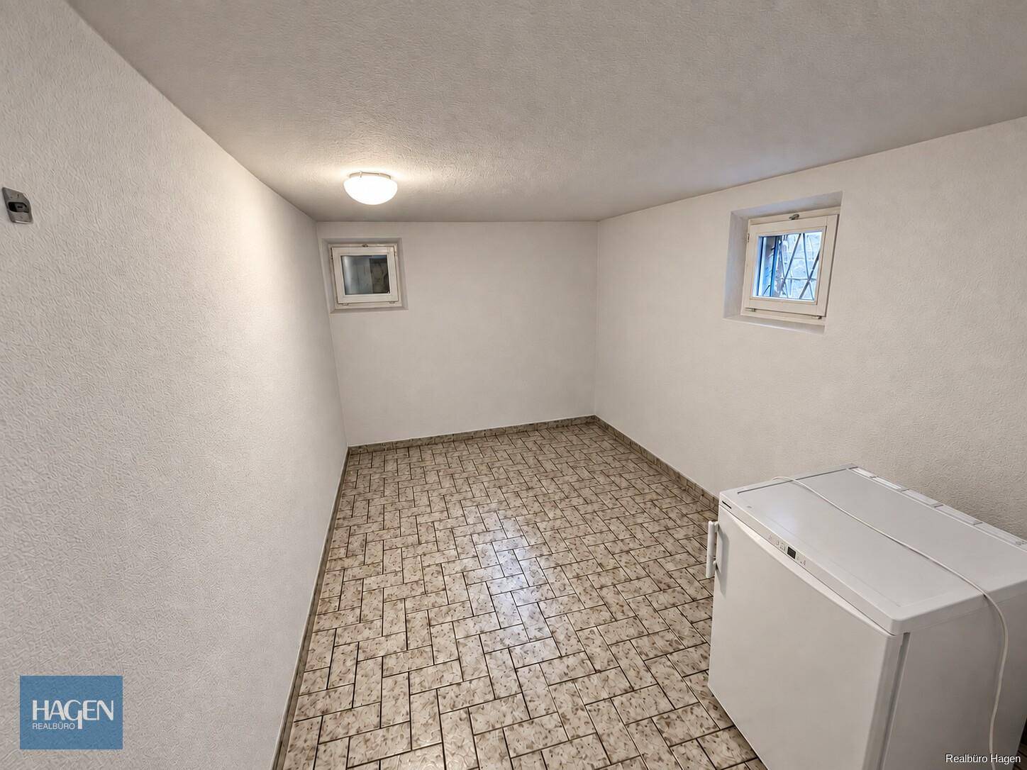 Kellerraum mit Fliesenboden, kleinem Fenster und Gefrierschrank.