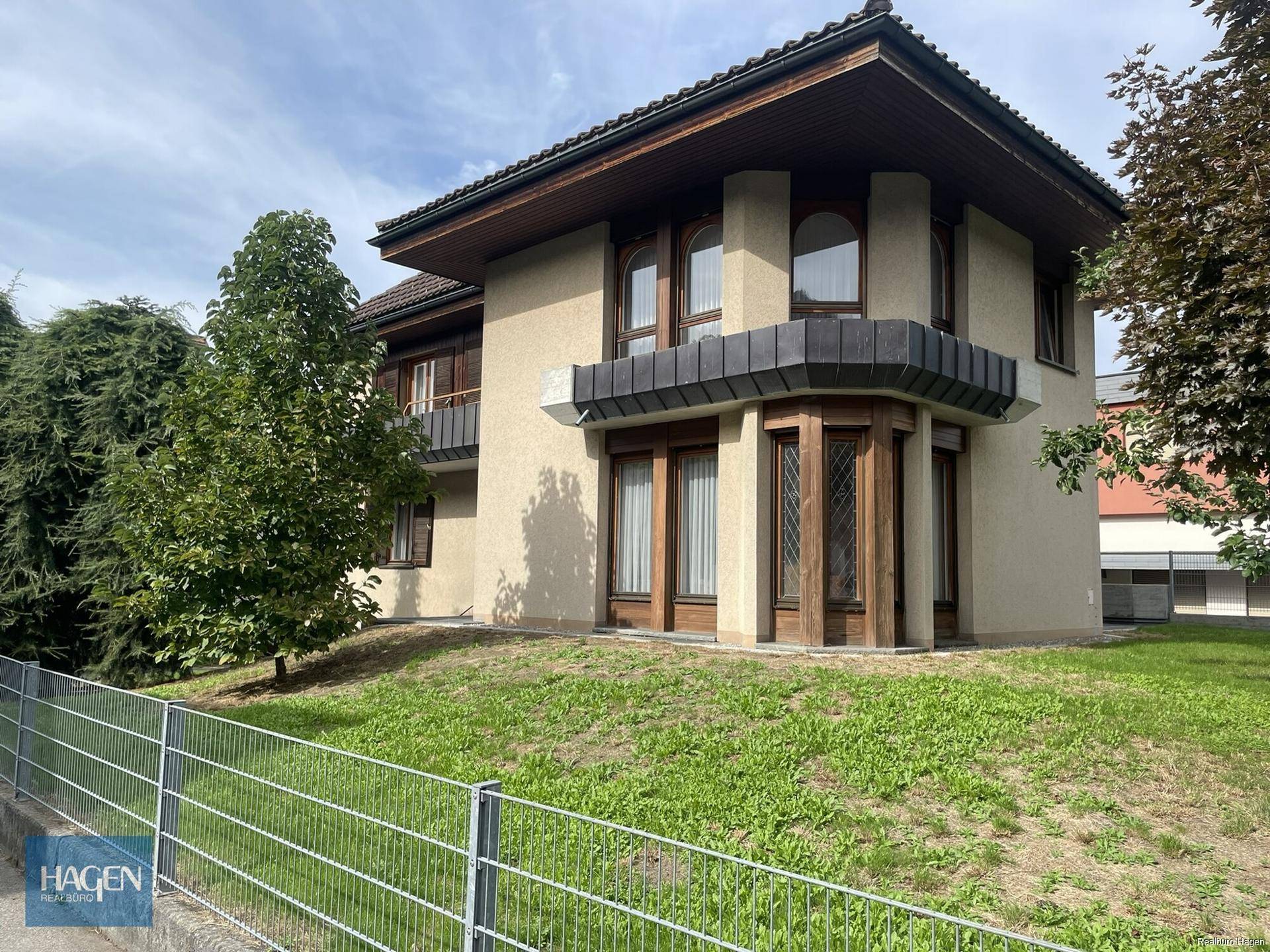 Seitenansicht des Hauses mit gepflegtem Rasen, Bäumen und einer klassischen Fassadengestaltung.