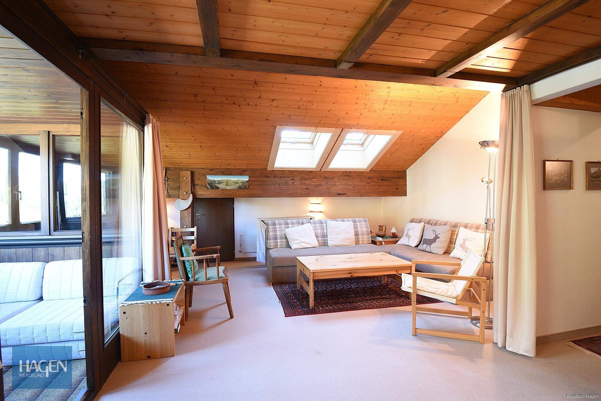 Helles Wohnzimmer mit Holzbalkendecke, gemütlichen Sofas und Blick auf die umliegende Natur.
