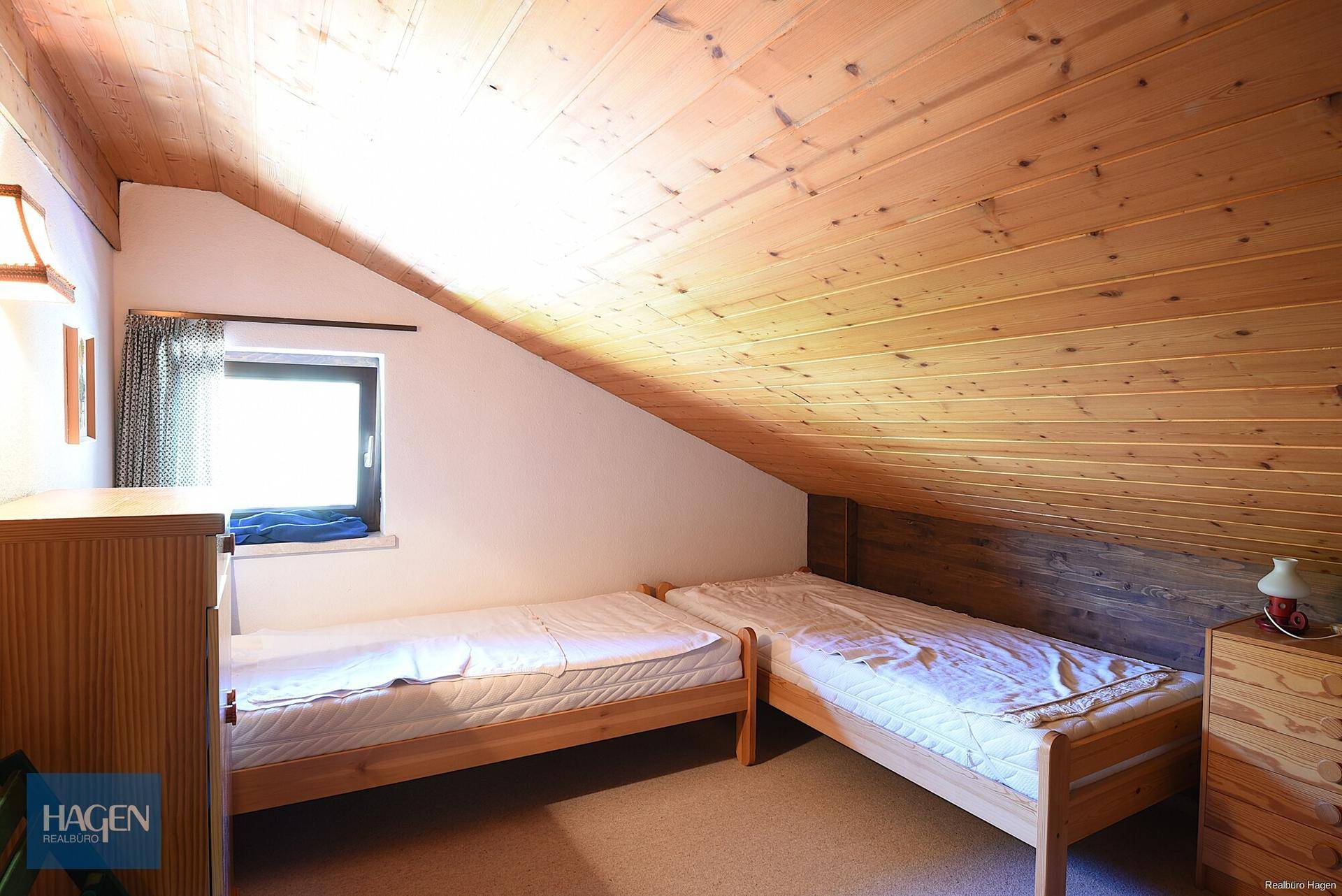 Helles Schlafzimmer mit zwei Einzelbetten, Dachschräge und Holzverkleidung an der Decke.