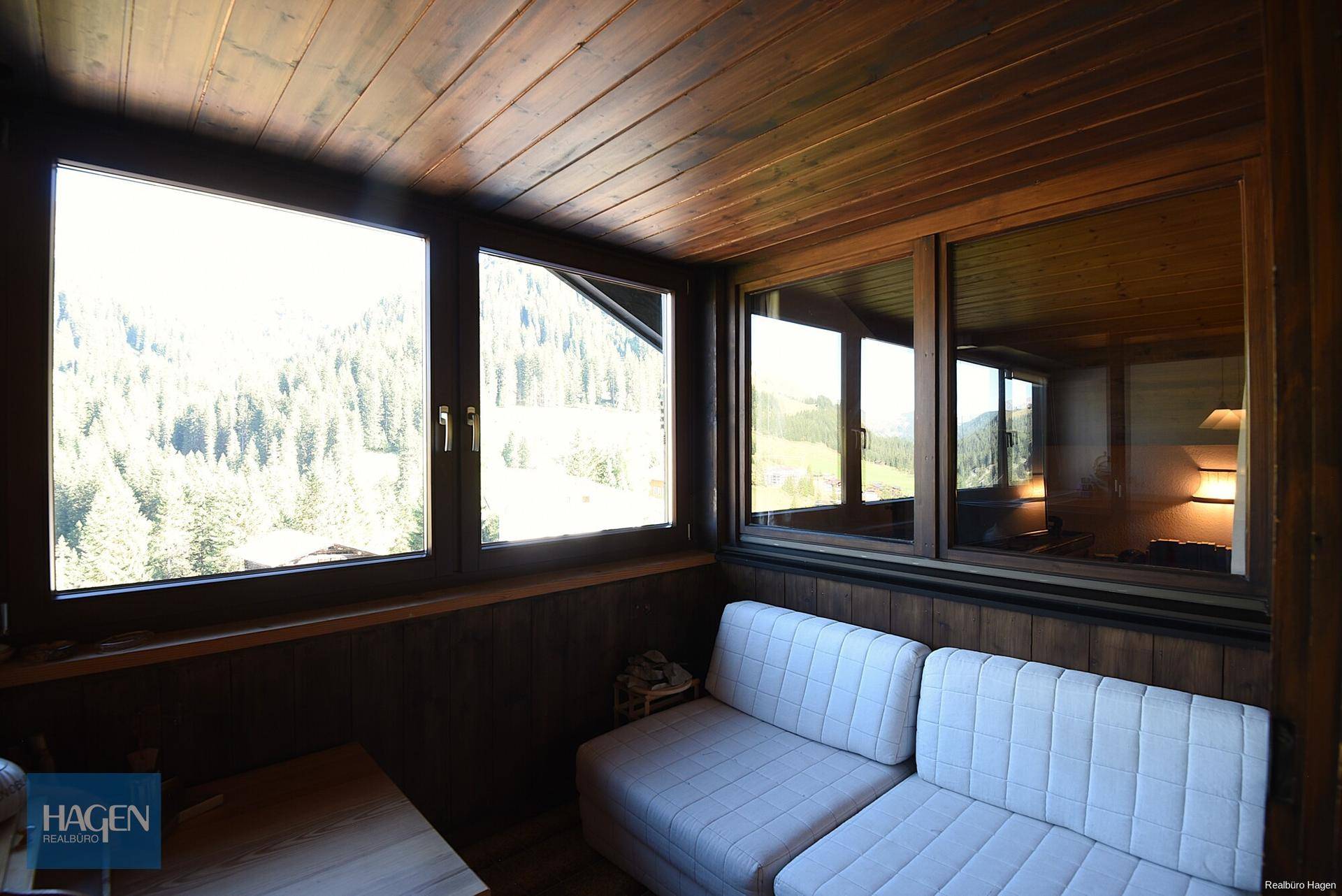 Heller Wintergarten mit bequemen Sofas und Panoramablick auf die umliegende Bergwelt.