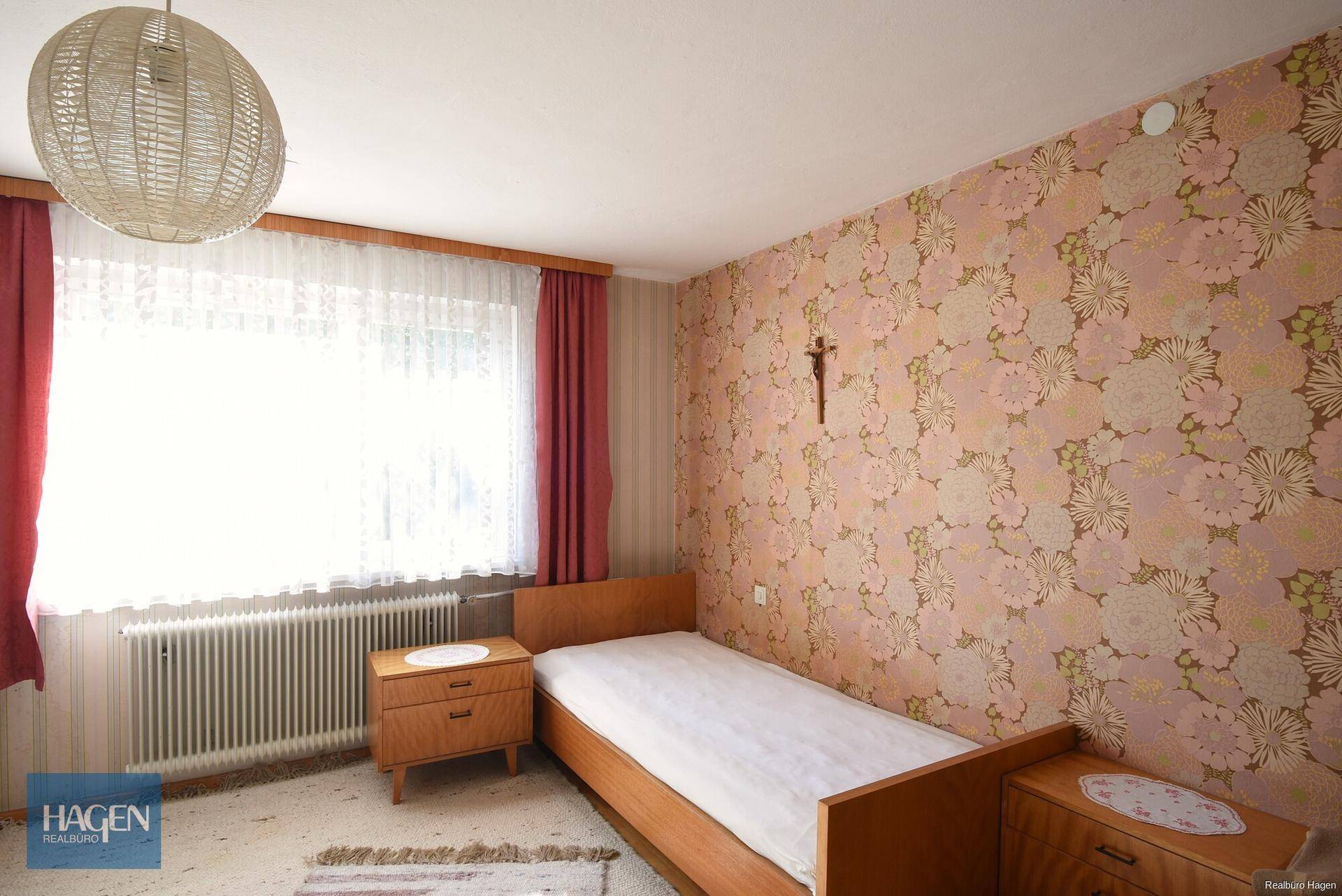 Schlafzimmer mit floraler Tapete, Einzelbett und großem Fenster.