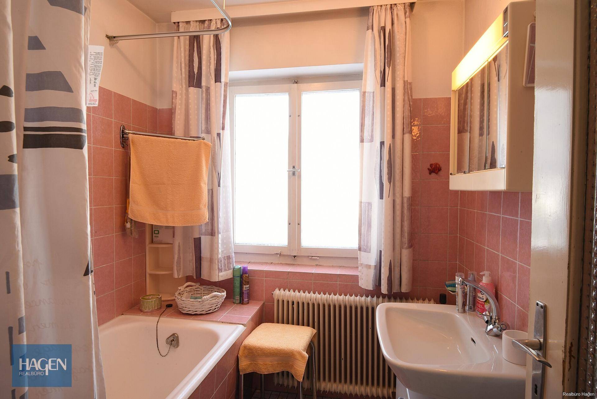 Badezimmer im 80er-Jahre-Stil mit rosa Fliesen, Badewanne und Fenster.
