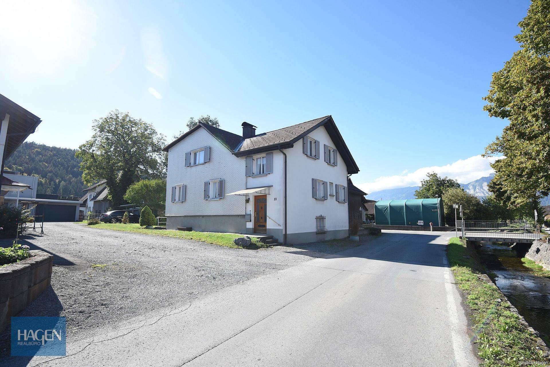Wohnhaus mit weißer Fassade, grauen Fensterläden und Blick auf die Berge.