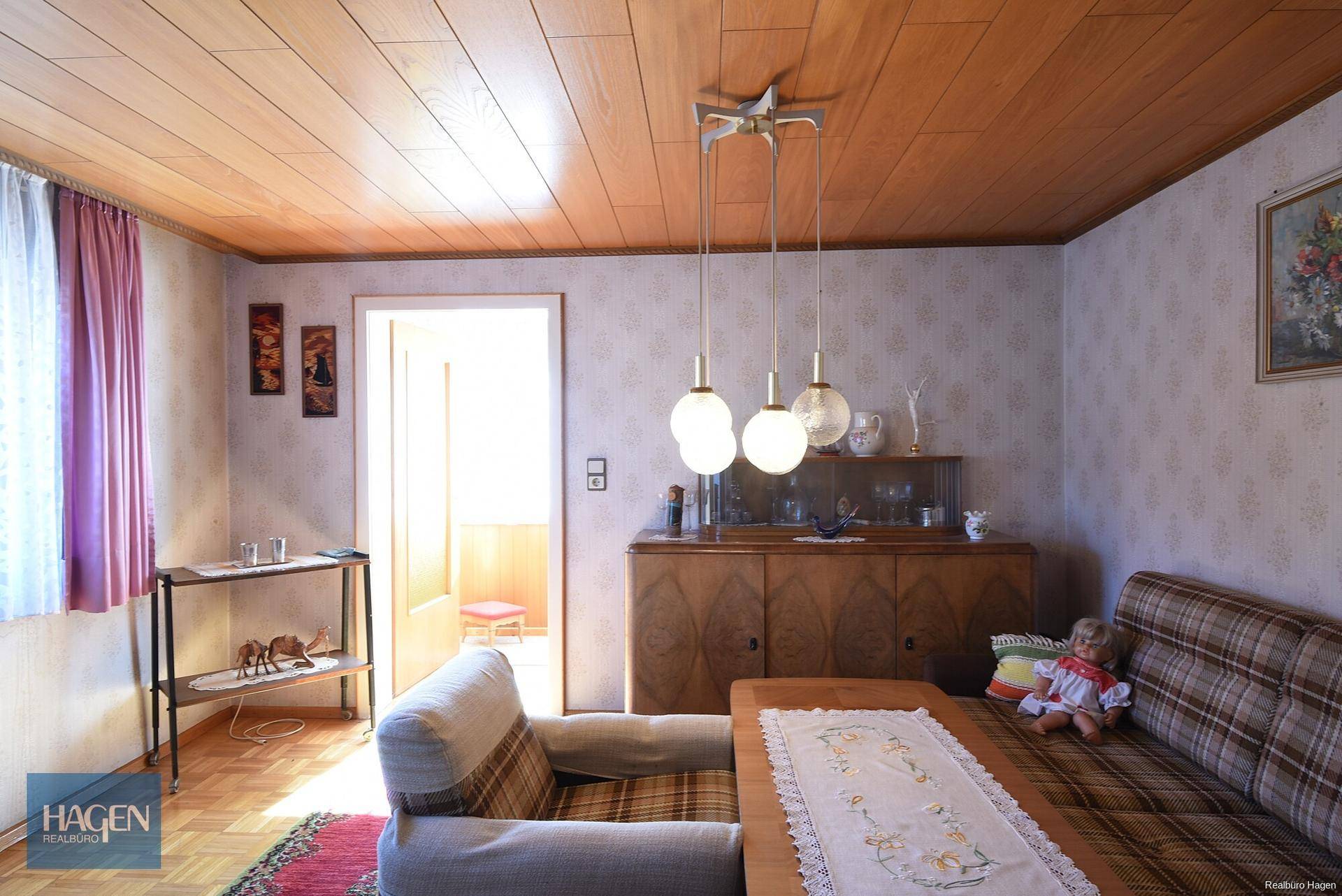 Wohnzimmer mit Holzdecke, gemusterter Tapete und traditionellen Möbeln.
