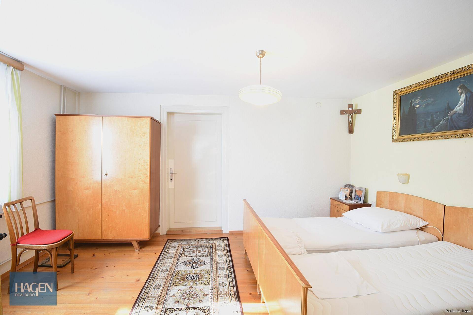 Helles Schlafzimmer mit zwei Einzelbetten, Holzschrank und Holzboden.