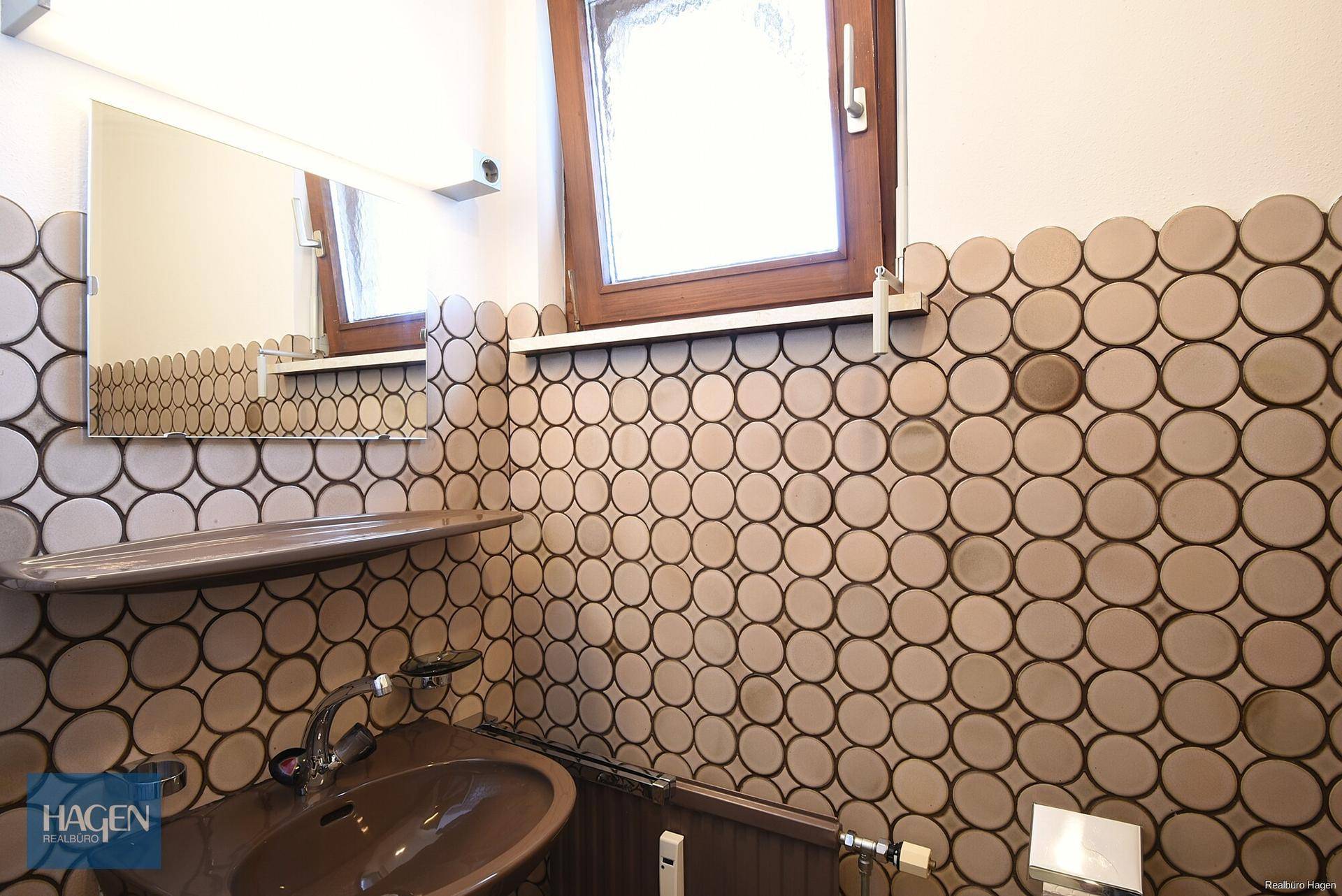 Gäste-WC mit runden Fliesen, Fenster und kleinem Waschbecken.