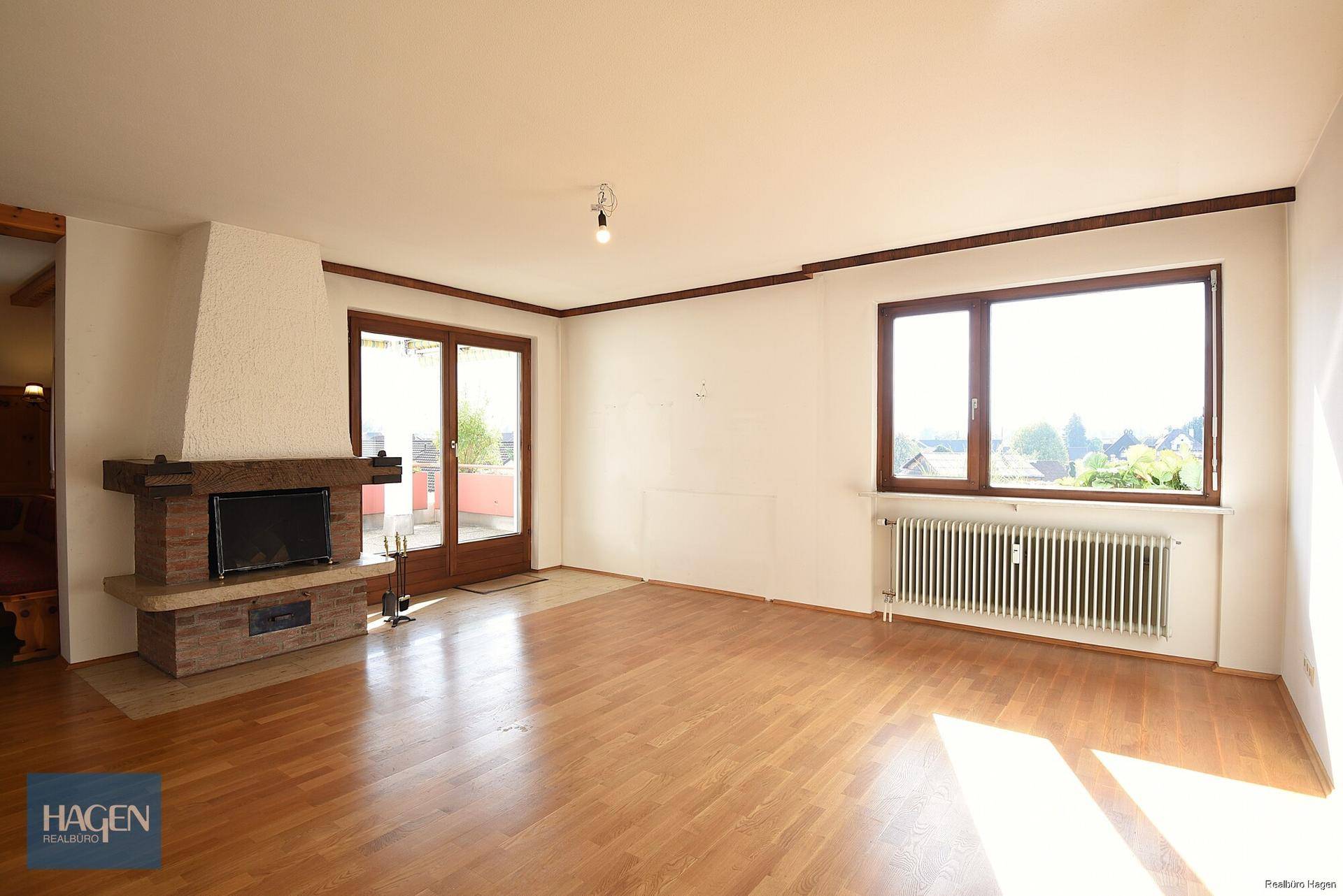 Helles Wohnzimmer mit Parkettboden, Kamin und großem Fenster mit Blick ins Grüne.