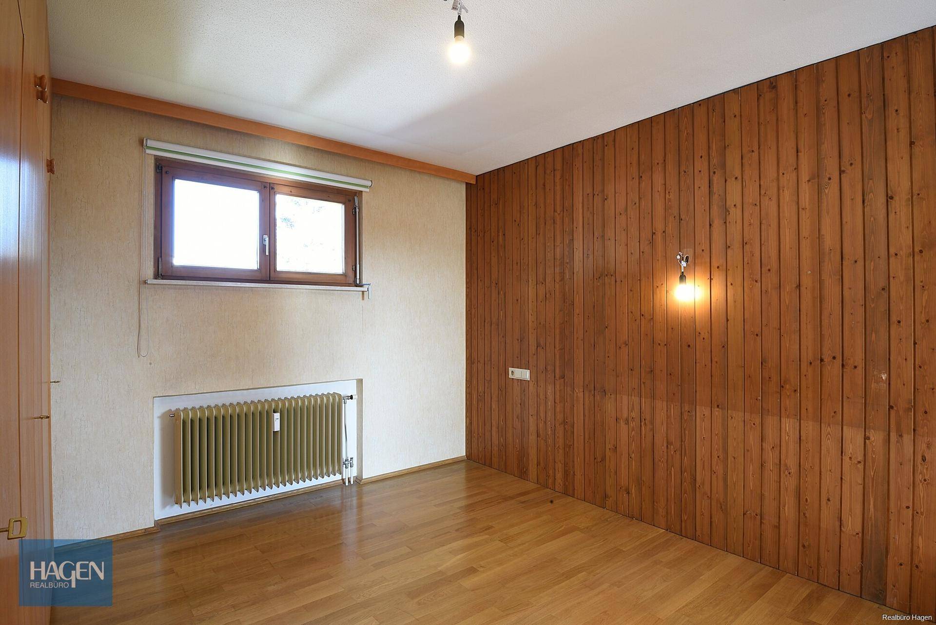 Schlafzimmer mit Holzwandverkleidung und Parkettboden, bietet eine warme Atmosphäre.
