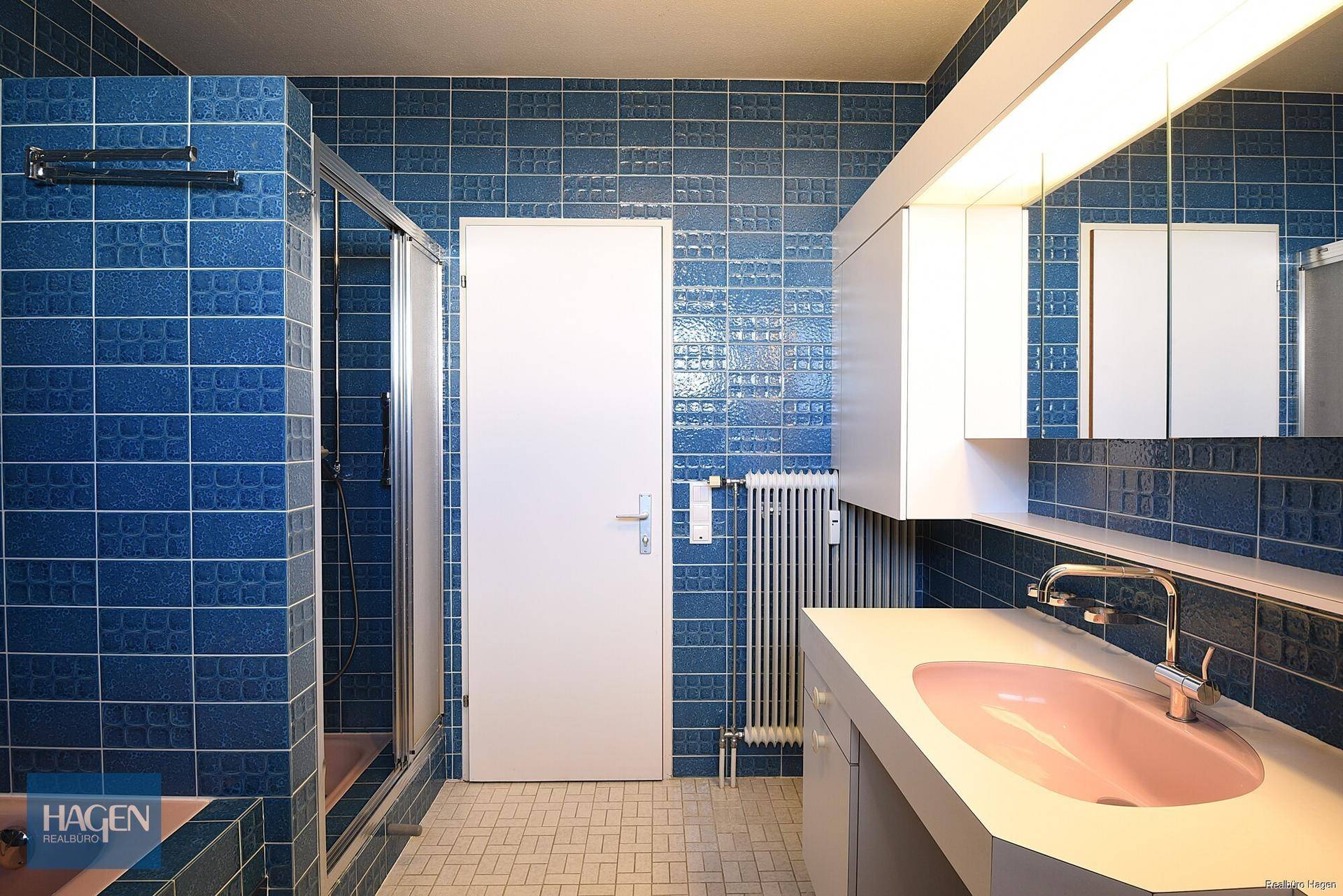 Badezimmer mit blauen Fliesen, Dusche und Waschtisch, funktional und hell.