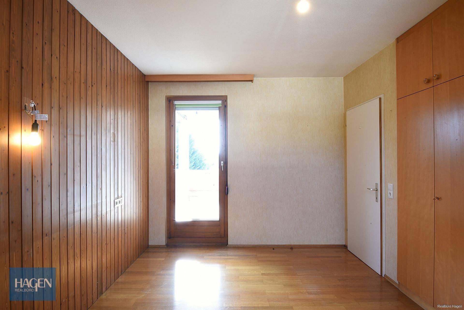 Schlafzimmer mit Holzwandverkleidung, Parkettboden und Zugang zum Balkon.