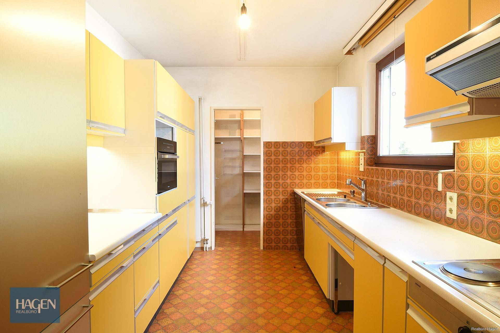 Küche im Retro-Stil mit gelben Schränken, gemusterten Fliesen und integrierter Speisekammer.
