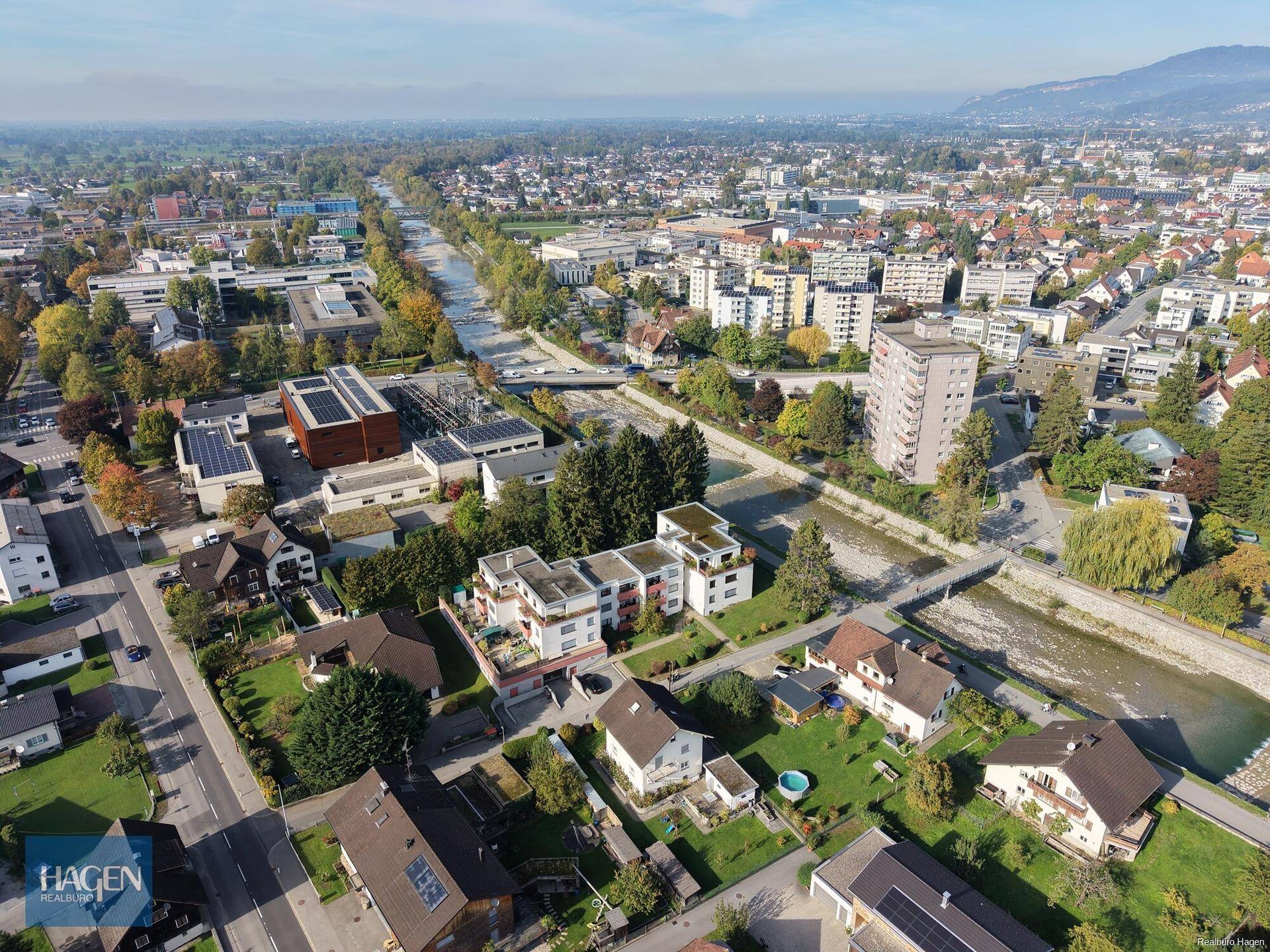 Weitläufige Luftaufnahme einer Siedlung mit Fluss und umliegender Landschaft.