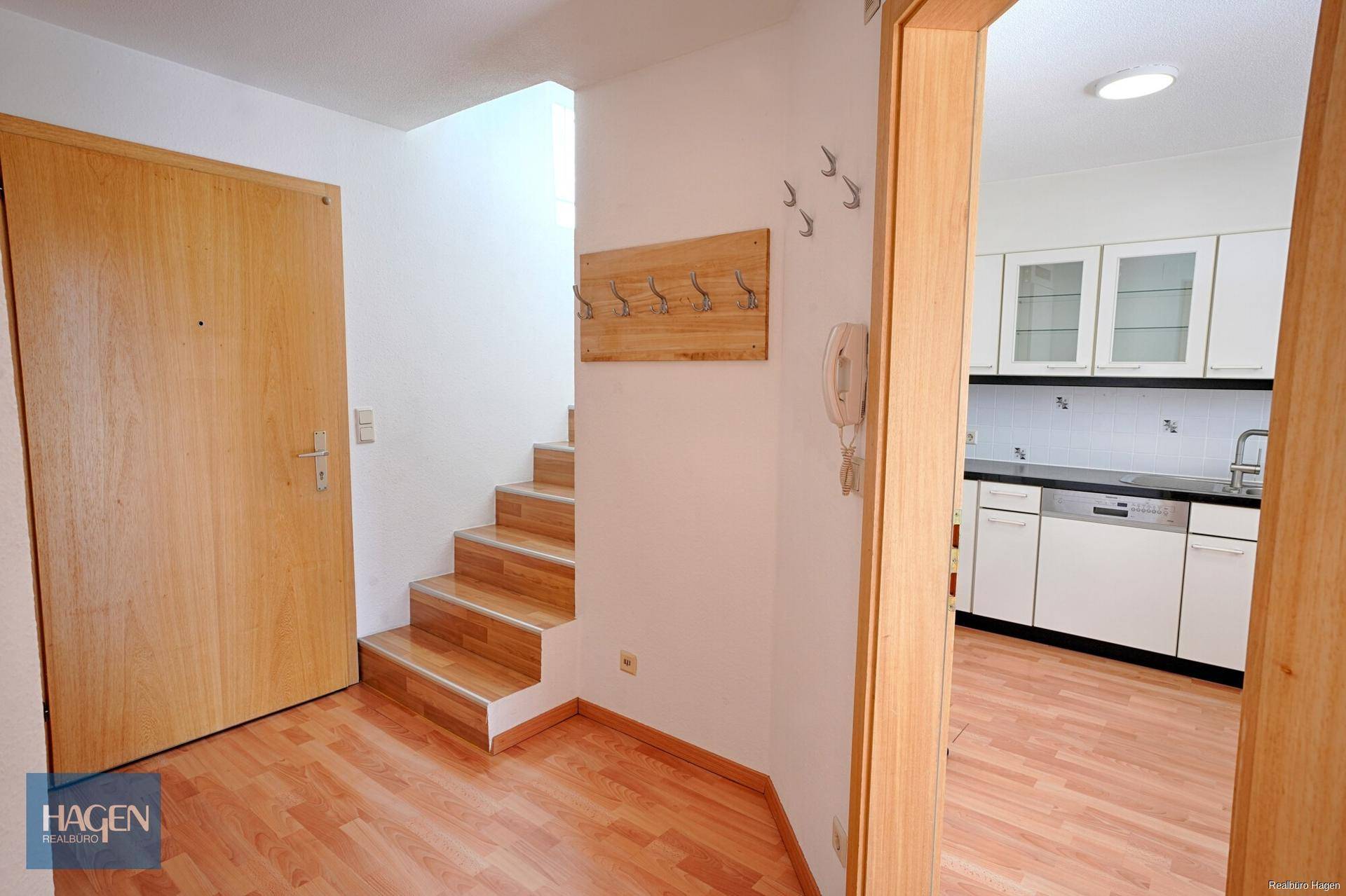 Heller Eingangsbereich mit Holztreppe und direktem Zugang zur Küche.
