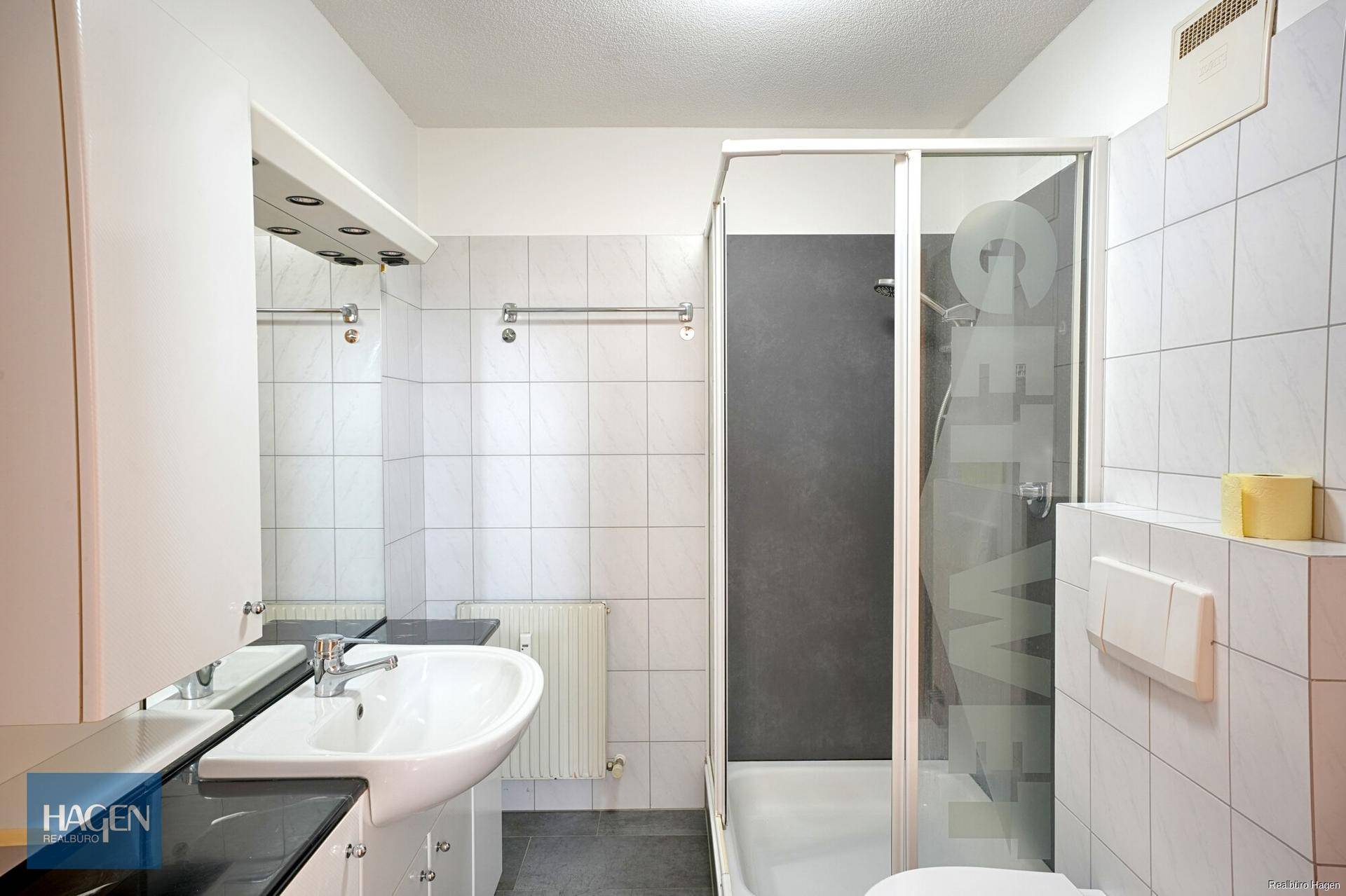 Helles Badezimmer mit Dusche, WC und weißen Wandfliesen.