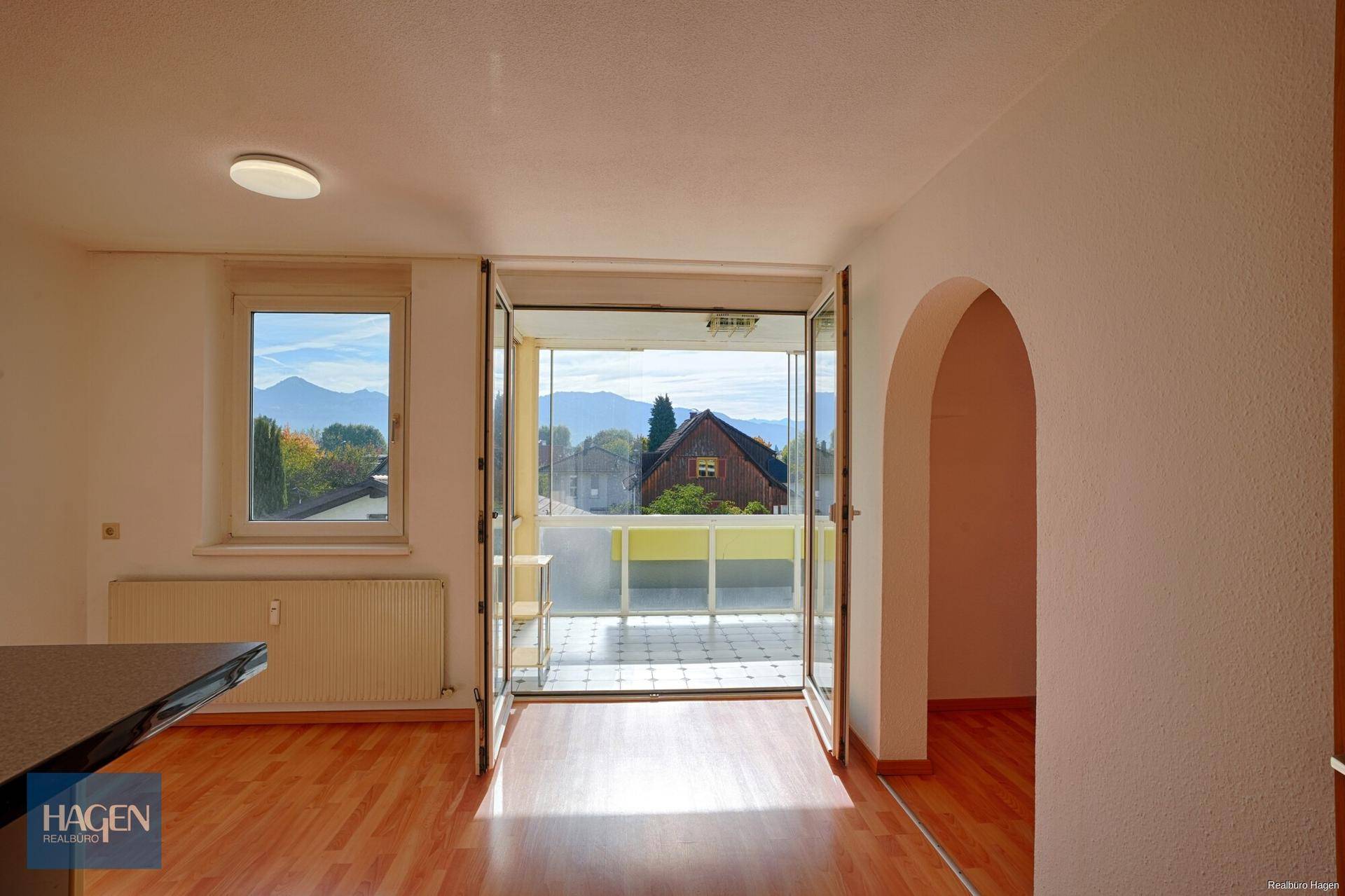 Heller Wohnbereich mit Zugang zum Balkon und weitem Blick auf die umliegende Berglandschaft.