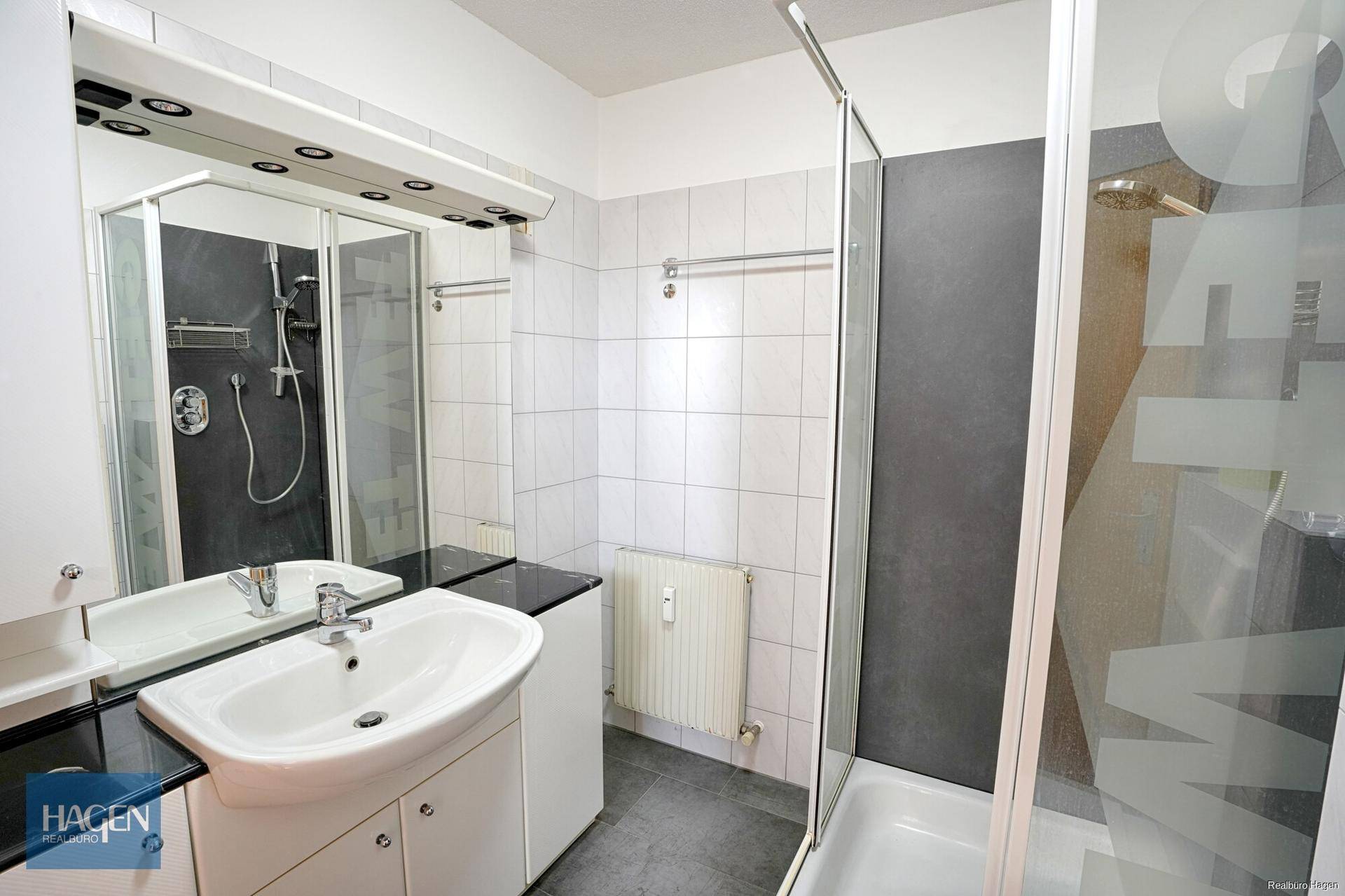 Modernes Badezimmer mit Dusche, Einzelwaschbecken und weißen Fliesen.