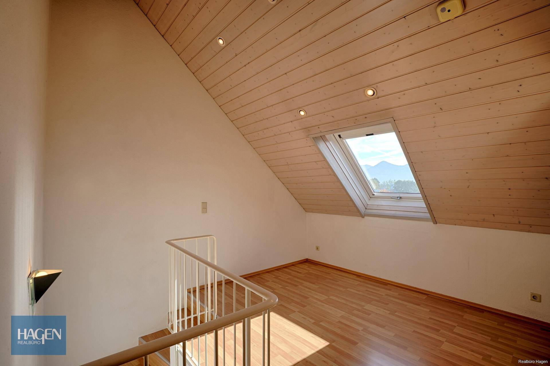 Dachgeschossraum mit Holzverkleidung, Dachfenster und Blick auf die Berge.