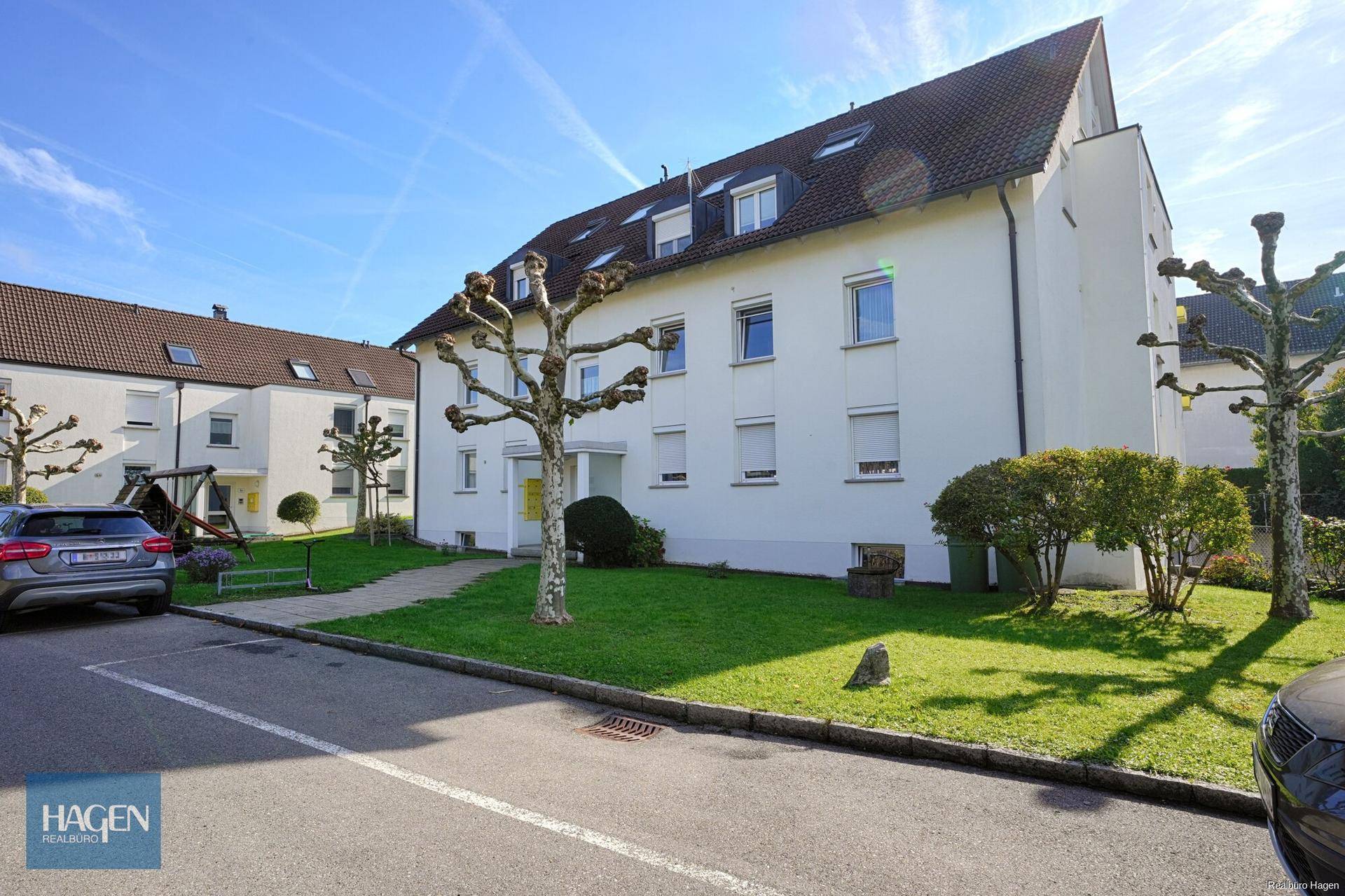 Wohngebäude mit weißer Fassade, gepflegter Außenanlage und Parkmöglichkeiten.