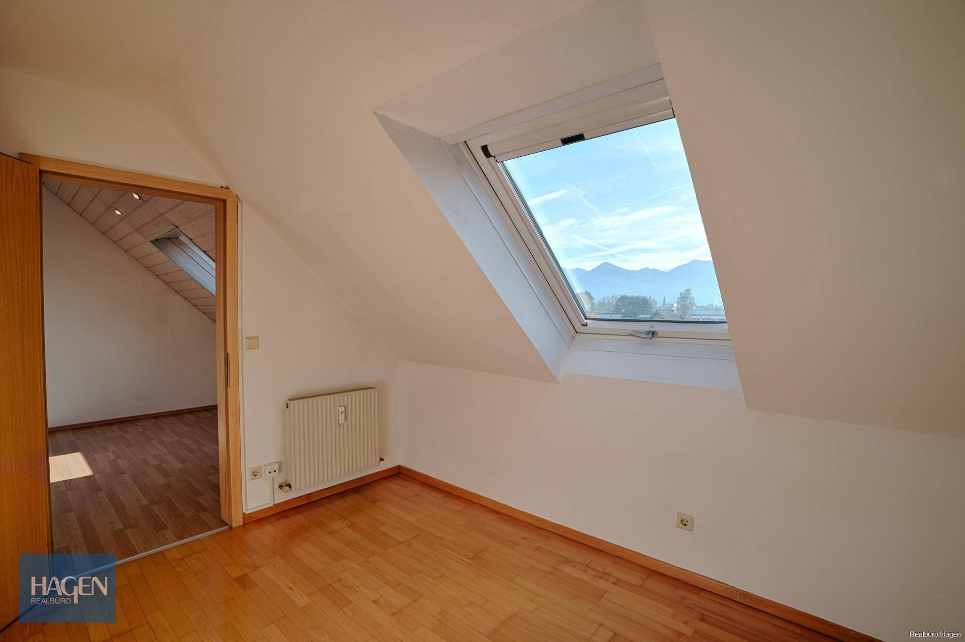 Dachzimmer mit großem Dachfenster, Parkettboden und Blick auf die Berglandschaft.