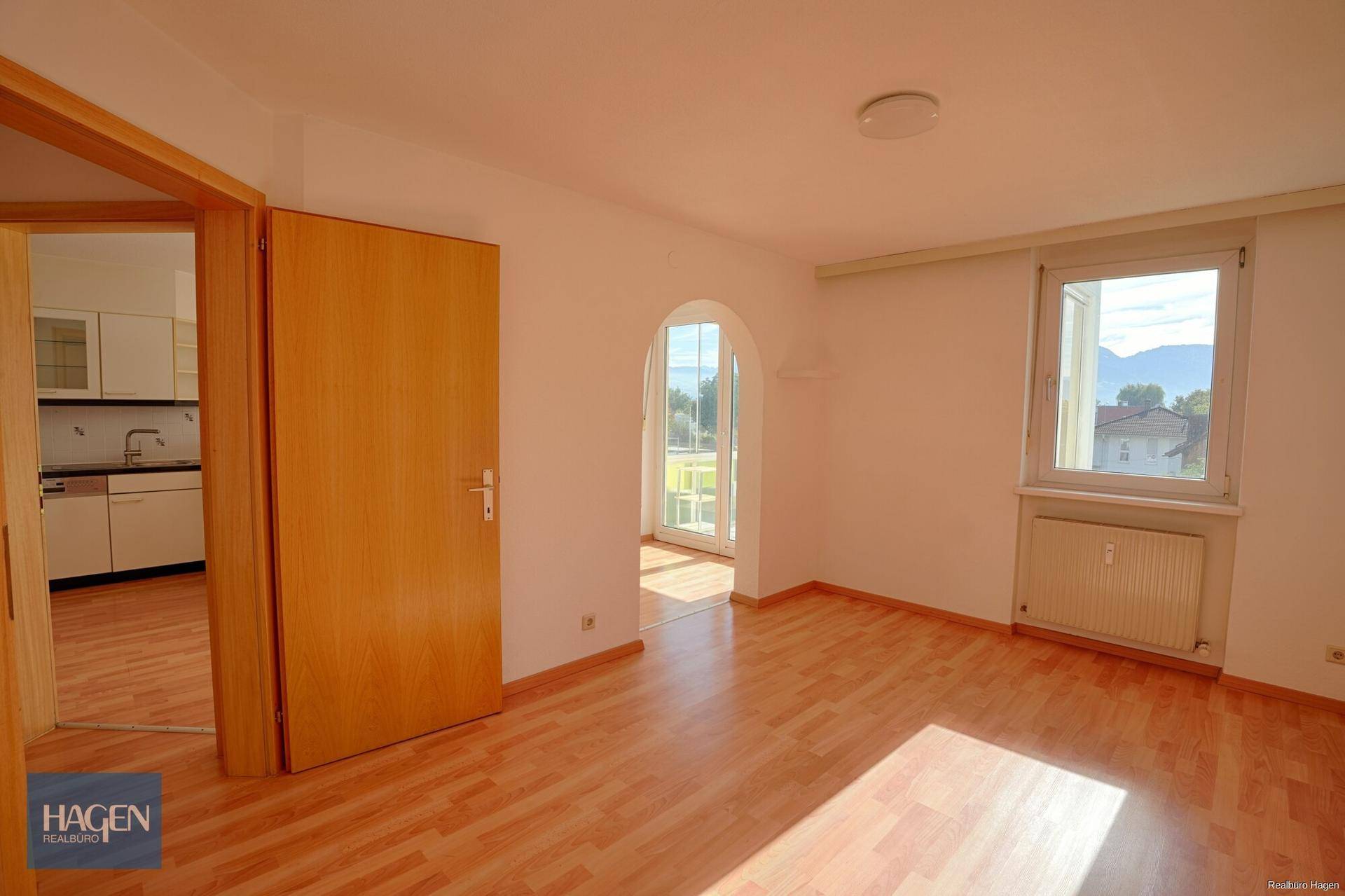 Geräumiger Wohnbereich mit Parkettboden, viel Tageslicht und Zugang zur Küche.