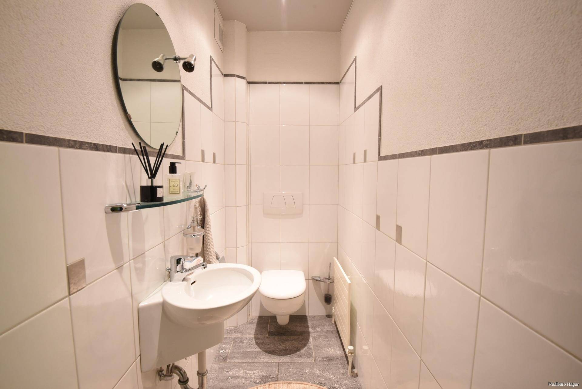 Kleines Gäste-WC mit Wand-WC, Waschbecken und Fliesen an Wänden und Boden.