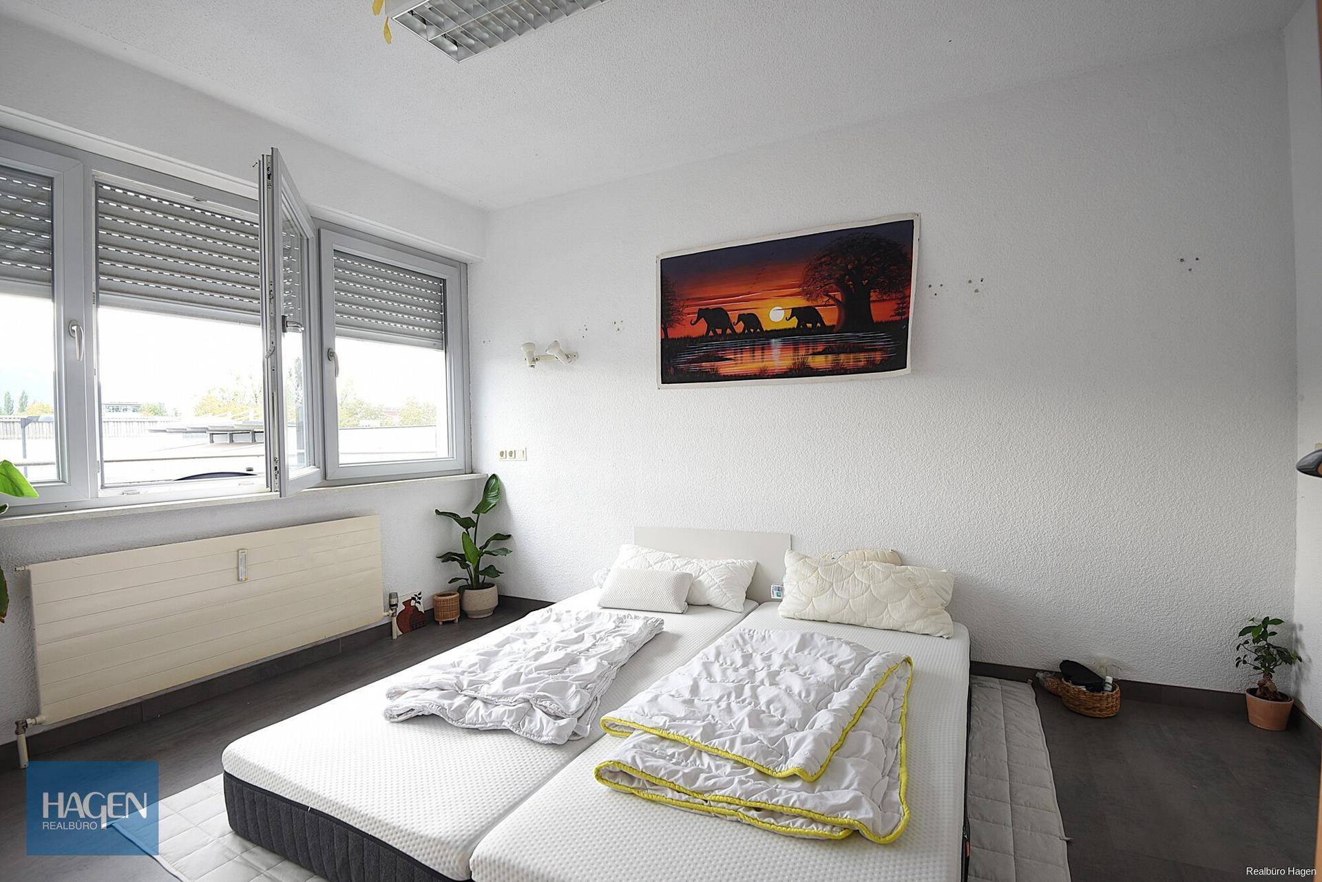 Helles Schlafzimmer mit zwei Einzelbetten, großen Fenstern und Rollläden.