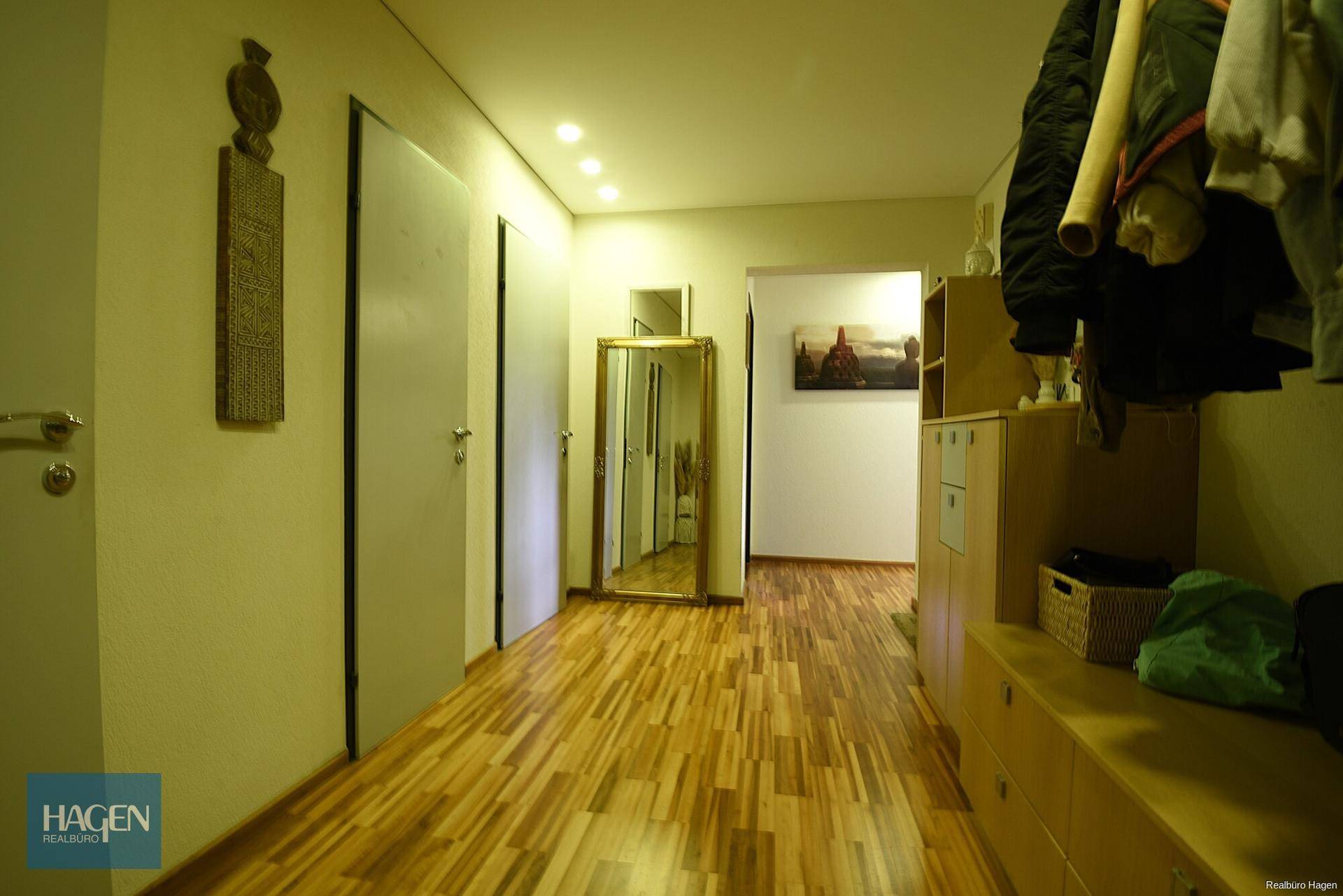 Heller Flur mit Holzparkettboden, Einbauschränken und einem großen Spiegel.