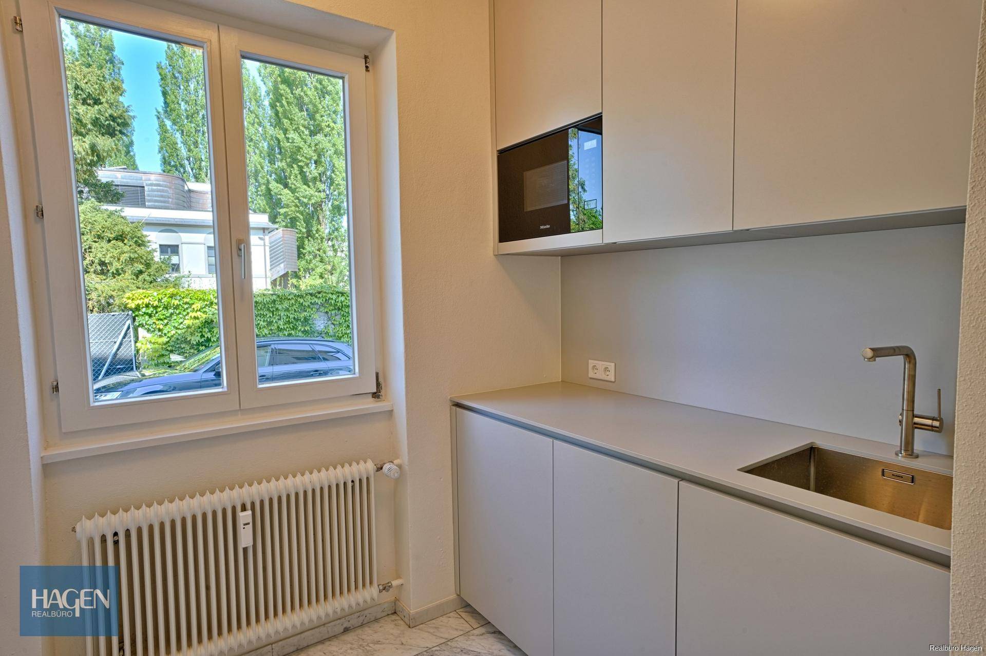 Kleine moderne Küche oder Kochnische mit grauen Schränken, Spüle und eingebauter Mikrowelle, mit Fenster.