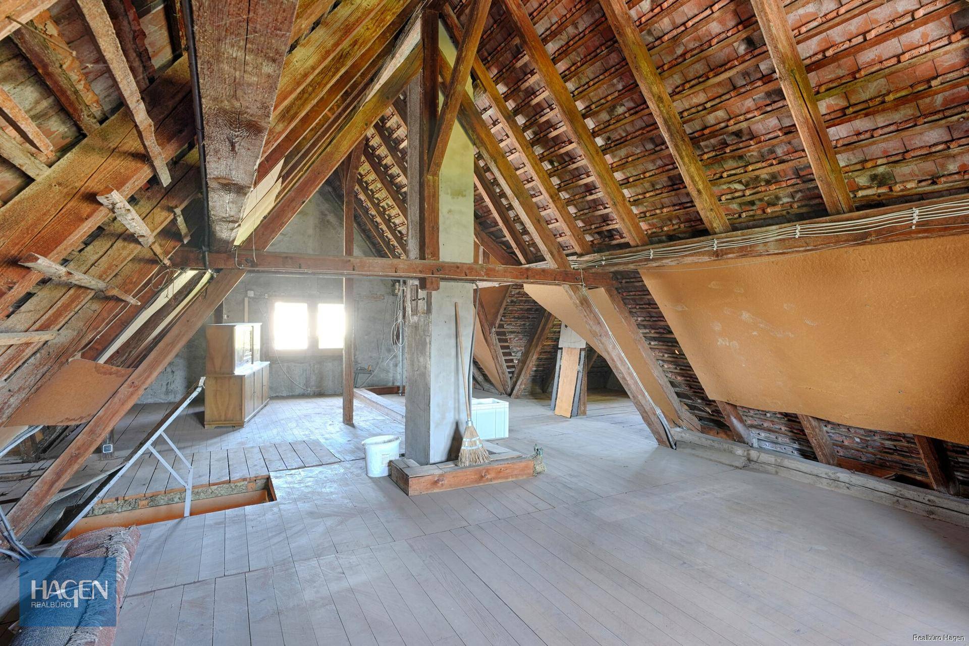 Geräumiger, unausgebauter Dachboden mit sichtbaren Holzbalken und Ziegeln.