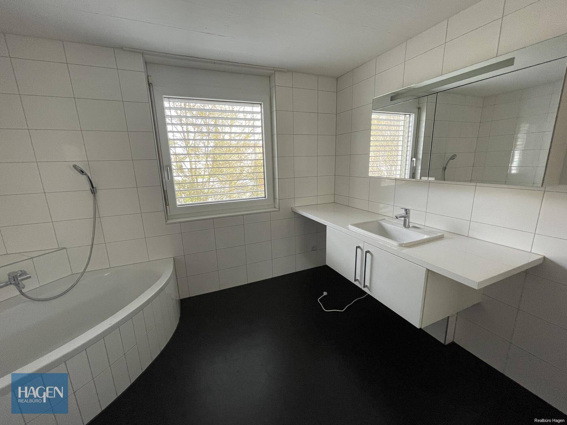 Modernes Badezimmer mit großem Waschtisch, Spiegel und Fenster, hell gefliest.