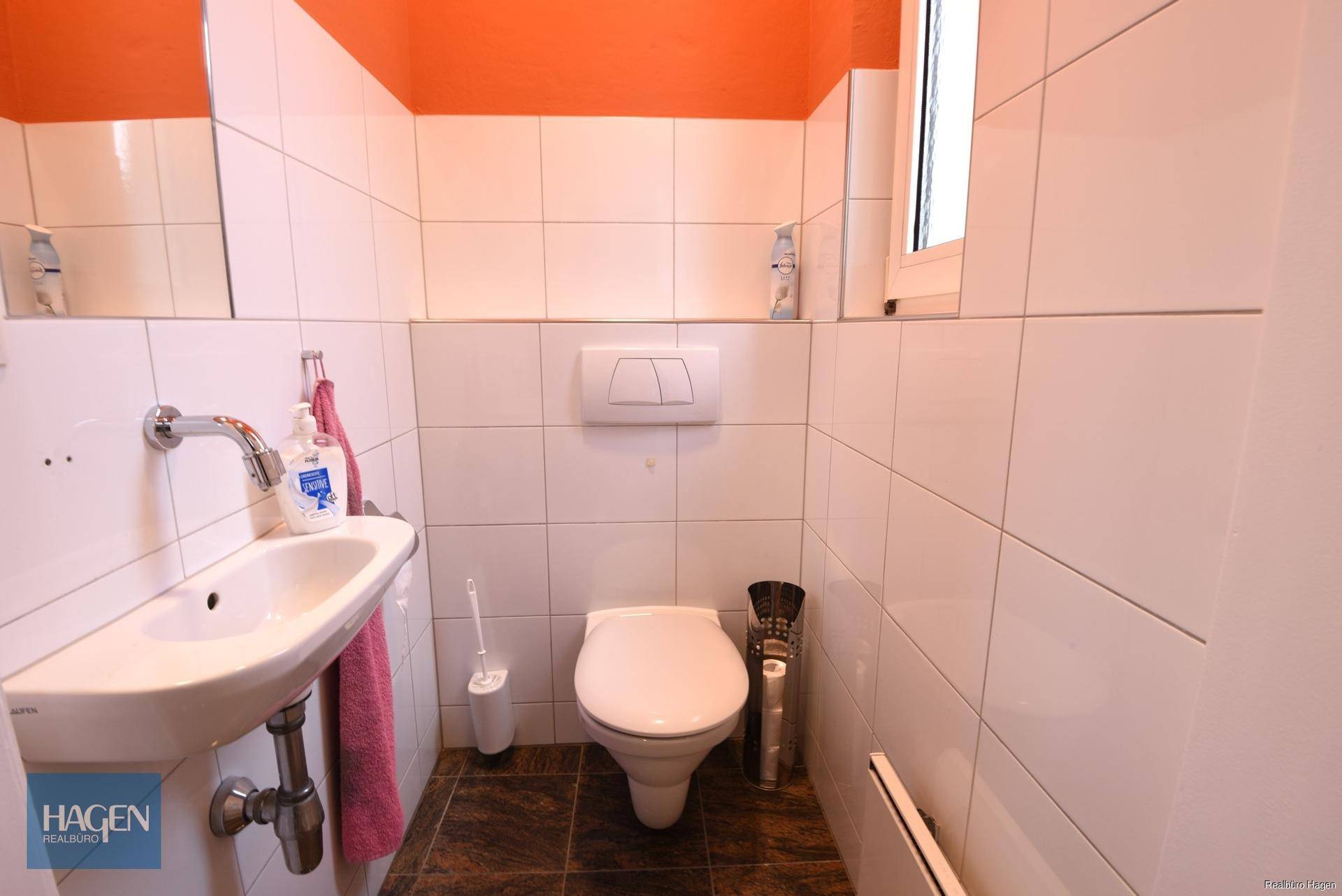 Kleine Gästetoilette mit weißen Fliesen, wandhängendem WC, kleinem Waschbecken und Fenster.
