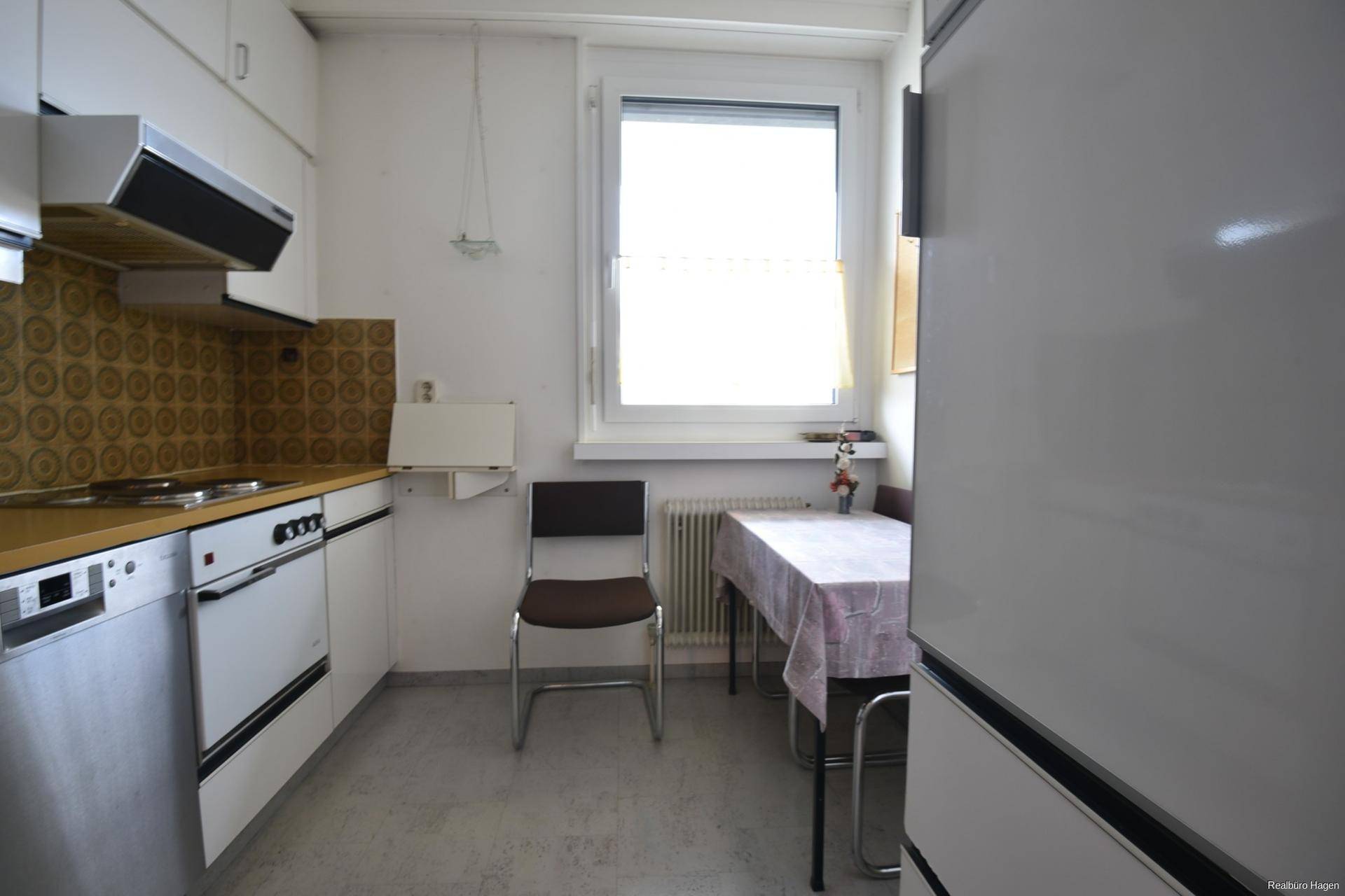 Kleine Küche mit weißen Schränken, älteren Geräten, einem Esstisch und einem Fenster.
