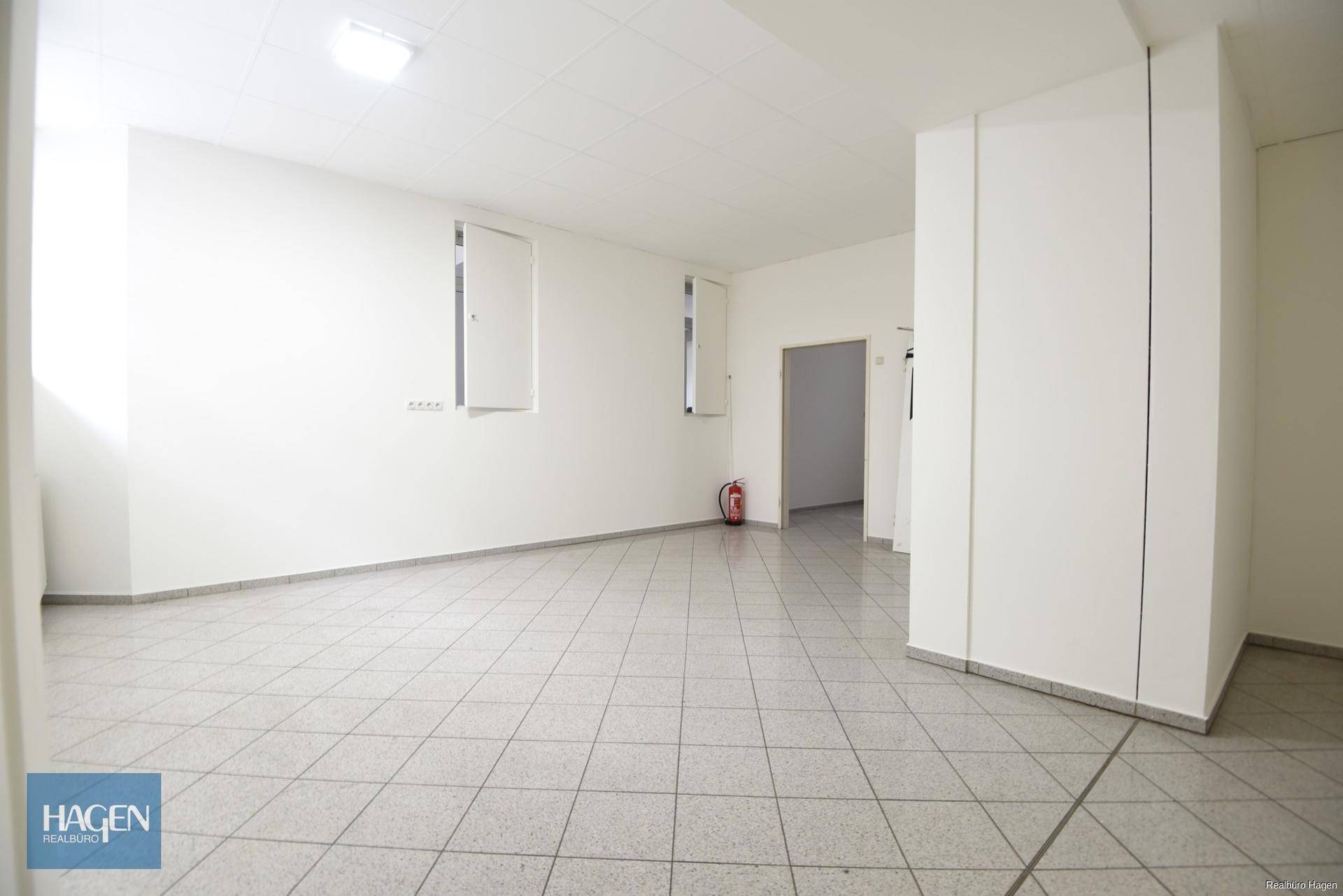 Heller Gewerberaum mit weißen Wänden, Fliesenboden und einem Feuerlöscher an der Wand.
