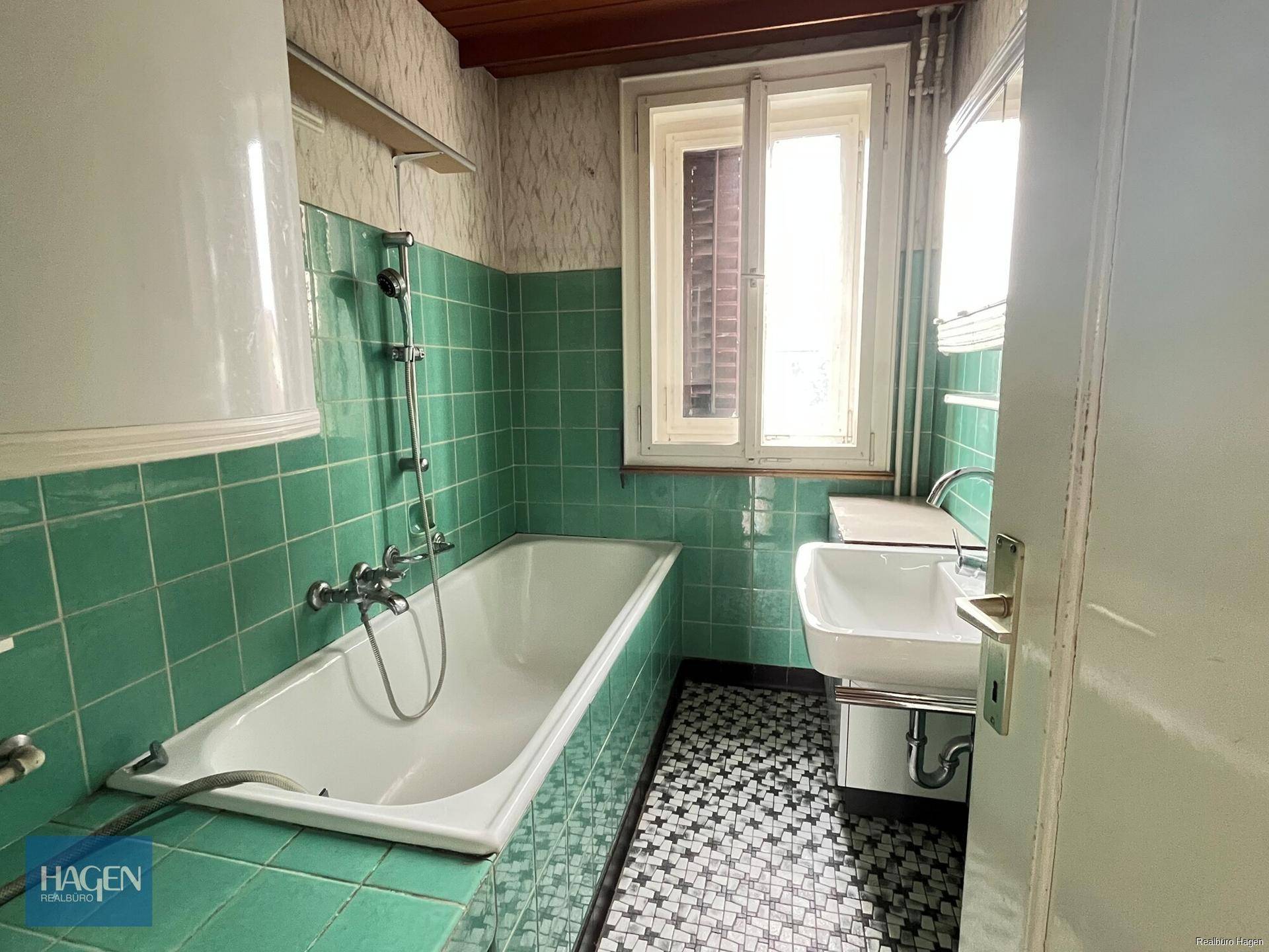 Badezimmer im Stil der 80er Jahre mit grünen Fliesen, Badewanne und Waschbecken.
