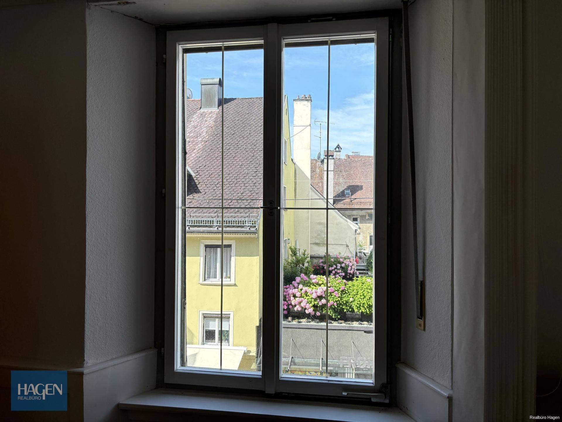 Fenster mit Blick auf einen begrünten Innenhof und umliegende Gebäude.