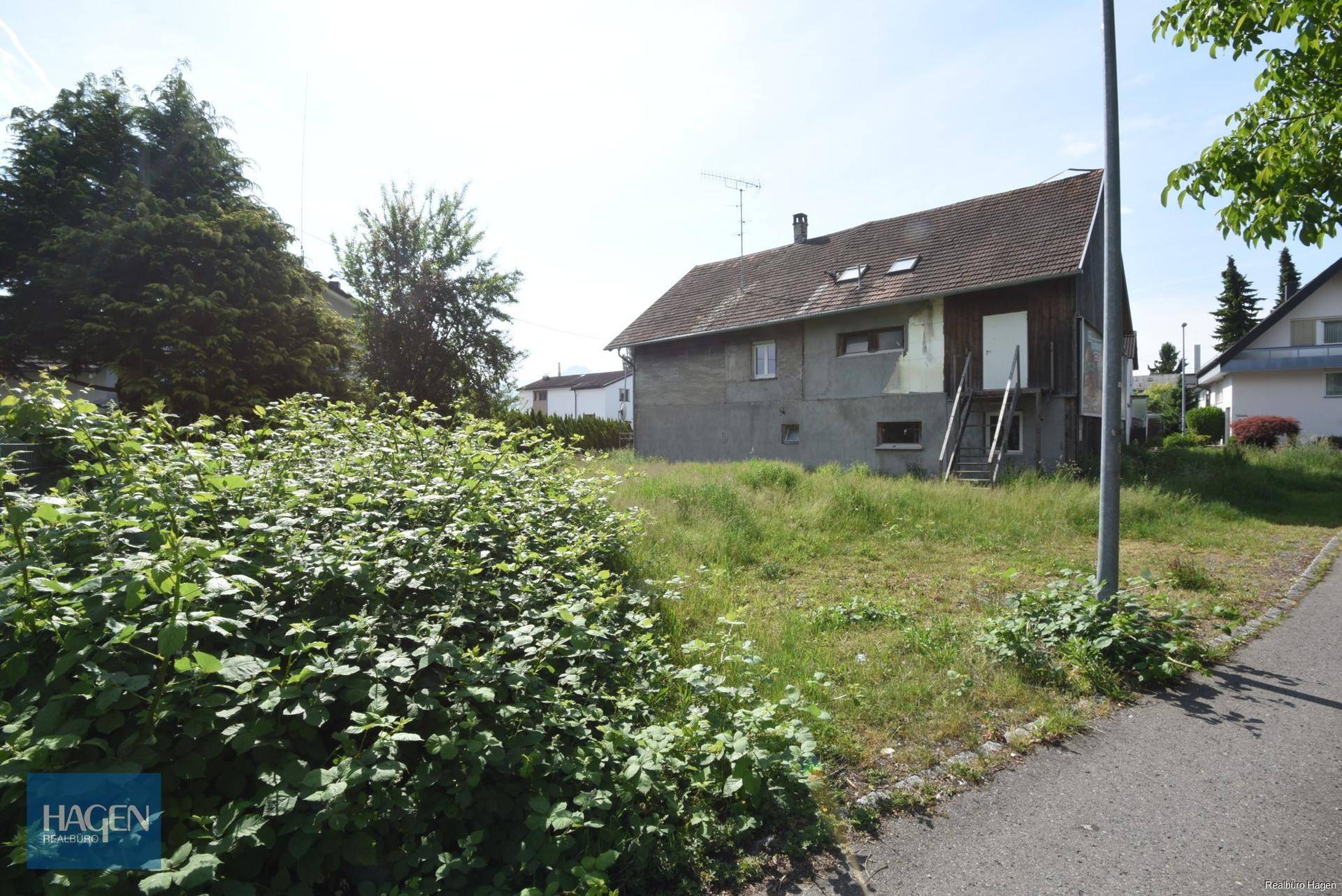Rückseite des Hauses mit ungepflegtem Grundstück und Außentreppe unter blauem Himmel.