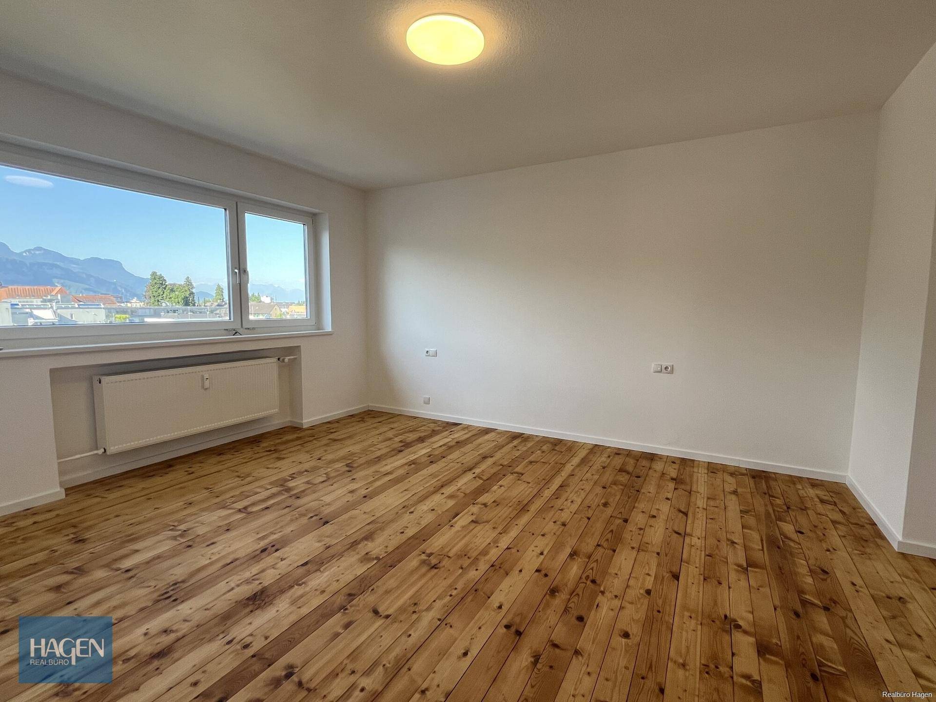 Helles Zimmer mit Holzplankenboden und weitem Blick auf die umliegende Landschaft und Berge.