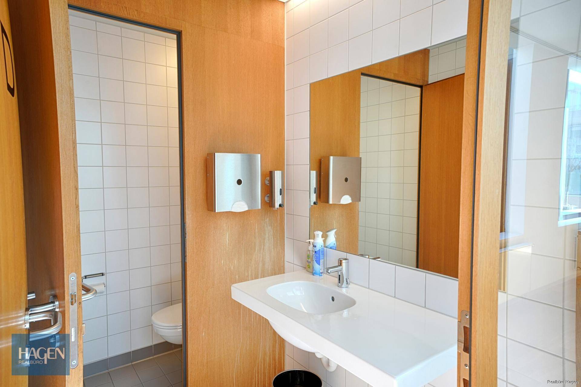 Saubere Toilette mit weißen Fliesen, Waschbecken und Holzverkleidung an den Wänden.