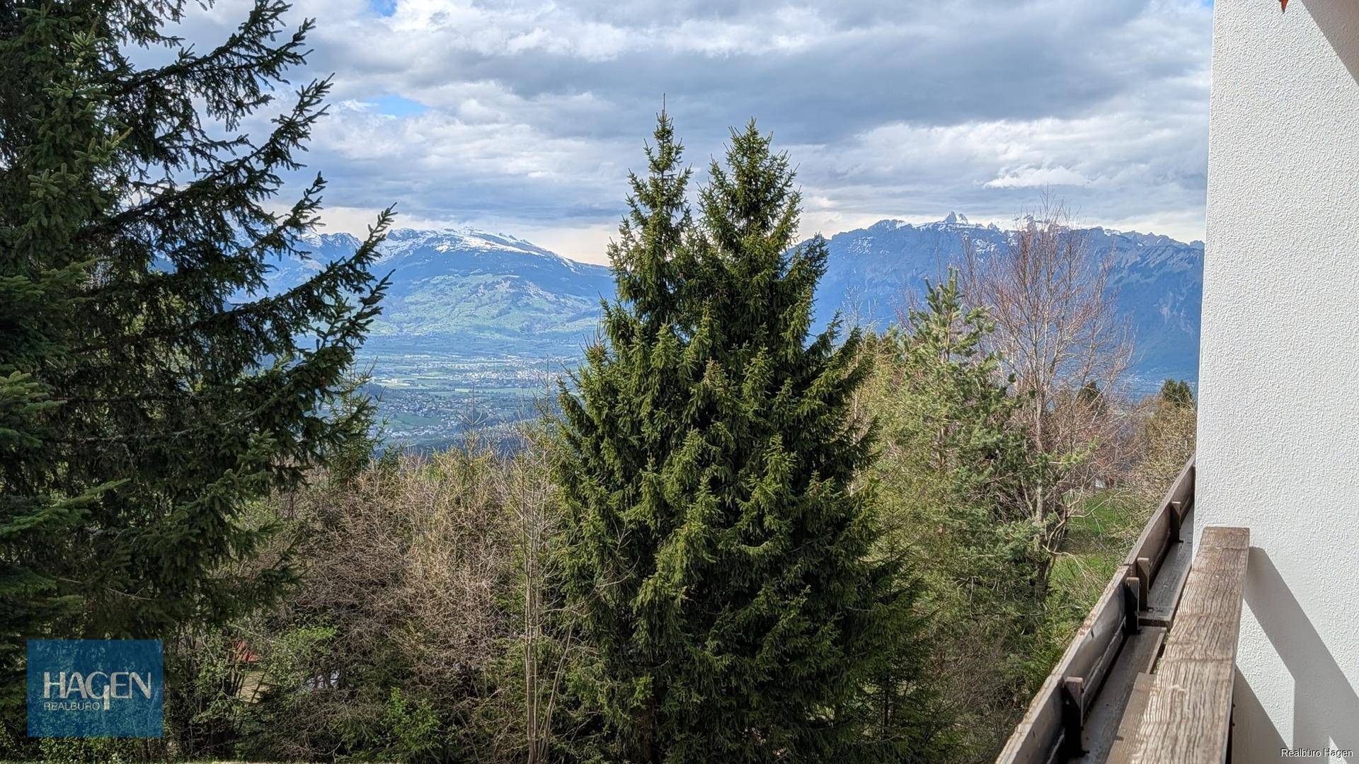 Malerischer Ausblick von einem Balkon auf die umliegenden Berge und das grüne Tal unter Wolken.