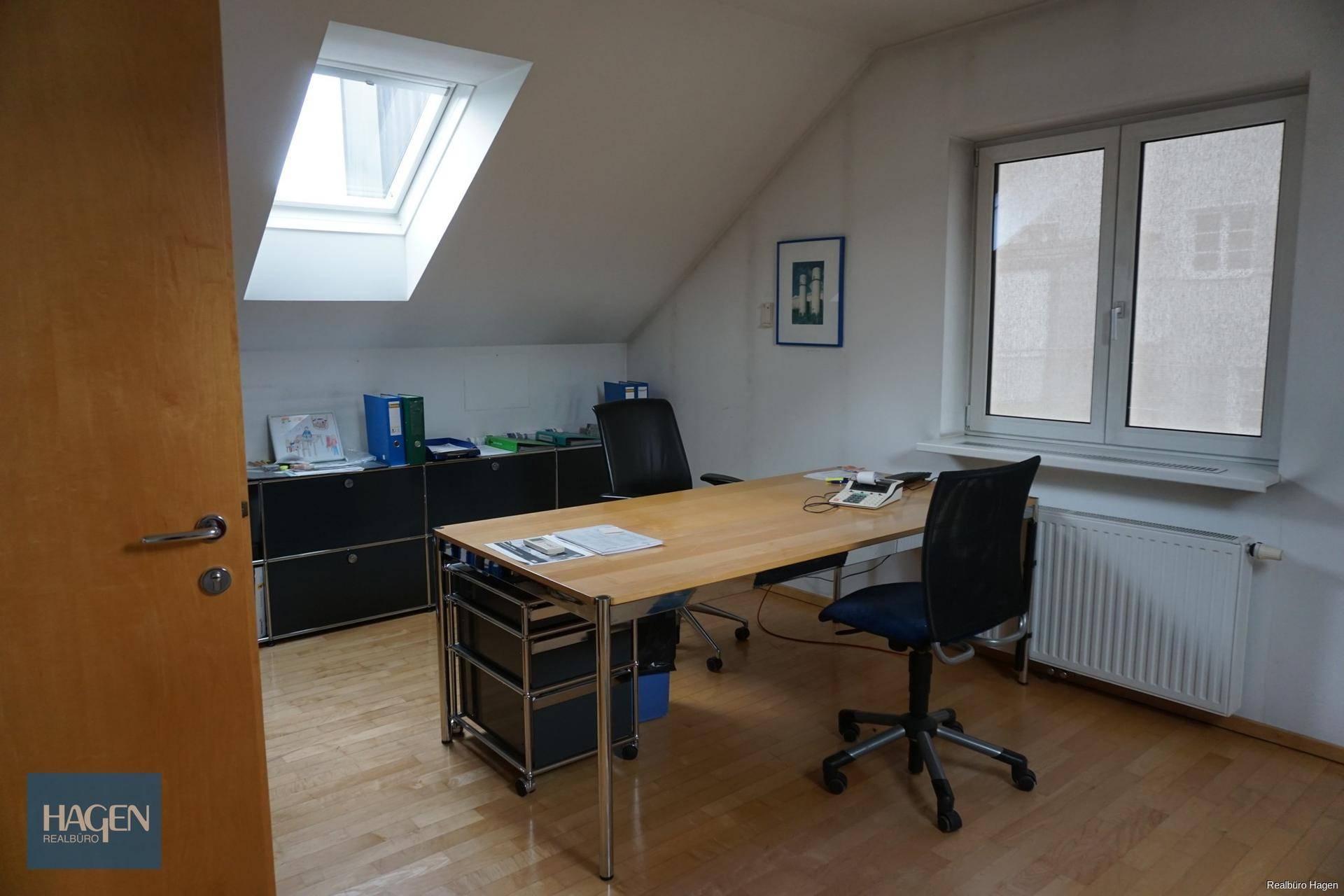 Helles Büro im Dachgeschoss mit Schreibtisch, Bürostühlen und Dachfenstern.