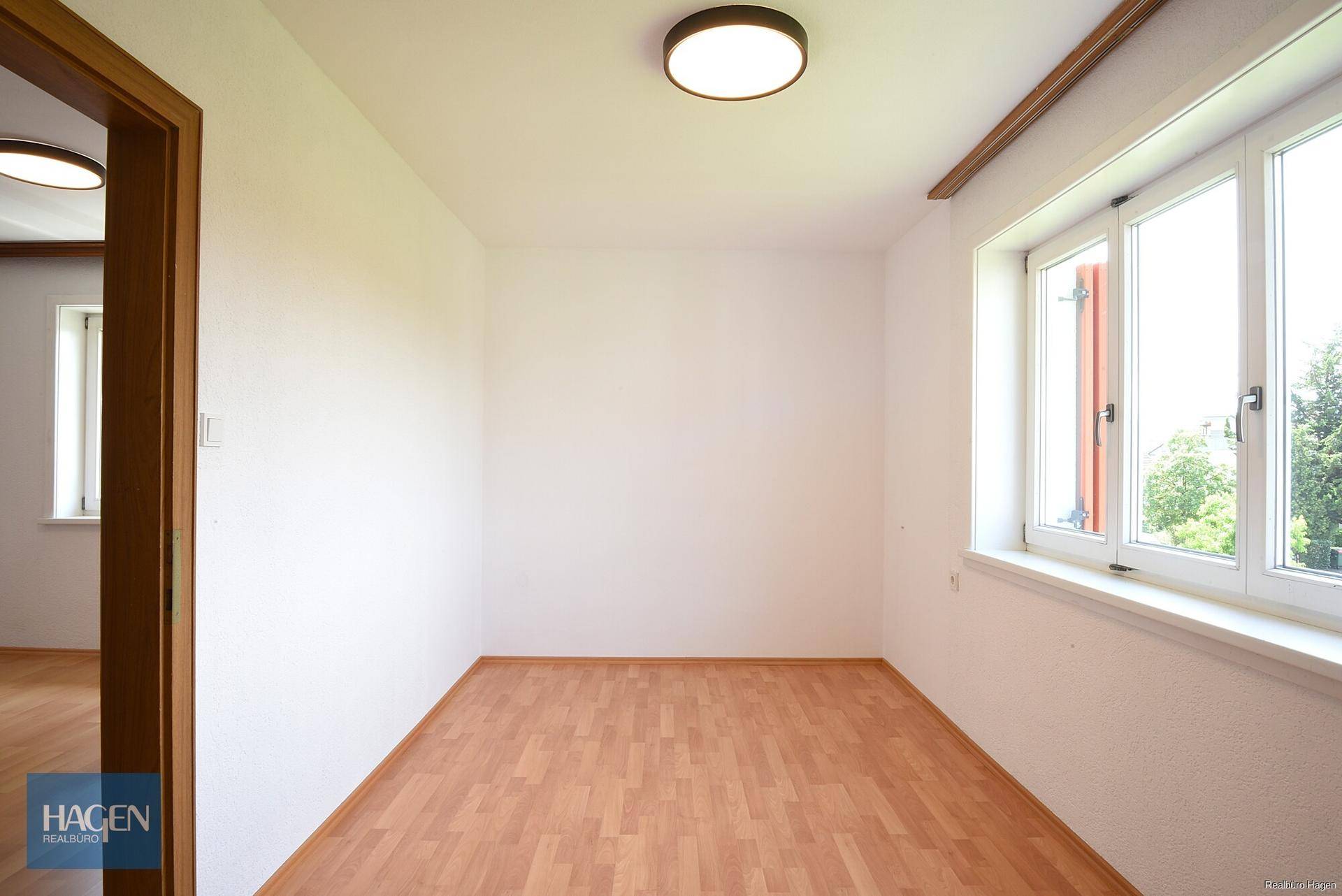 Freundliches Zimmer mit Laminatboden und Blick ins Grüne durch das Fenster, bietet viel Tageslicht.
