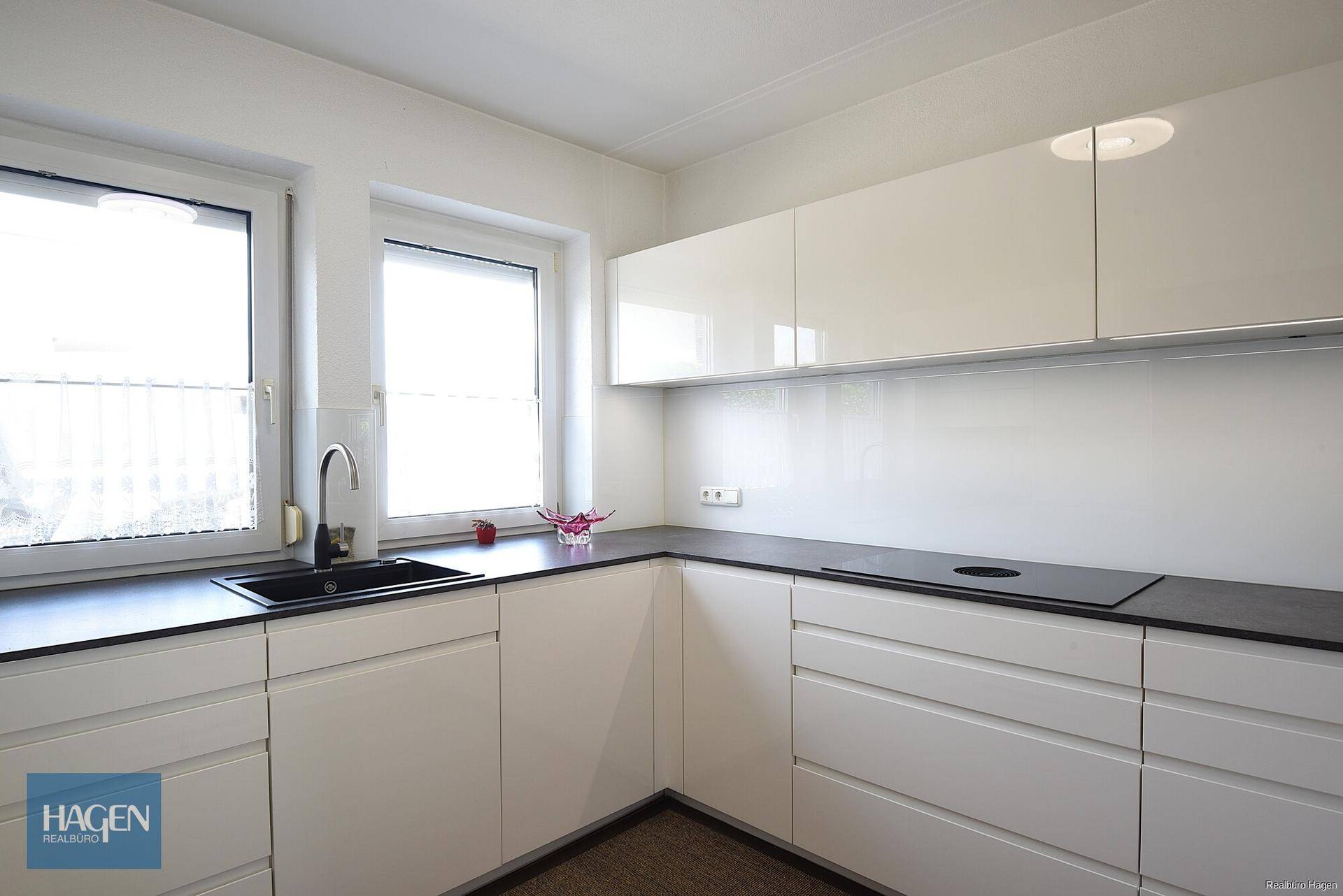 Moderne Küche mit weißen Hochglanzschränken, dunkler Arbeitsplatte, Induktionskochfeld und Fenster.
