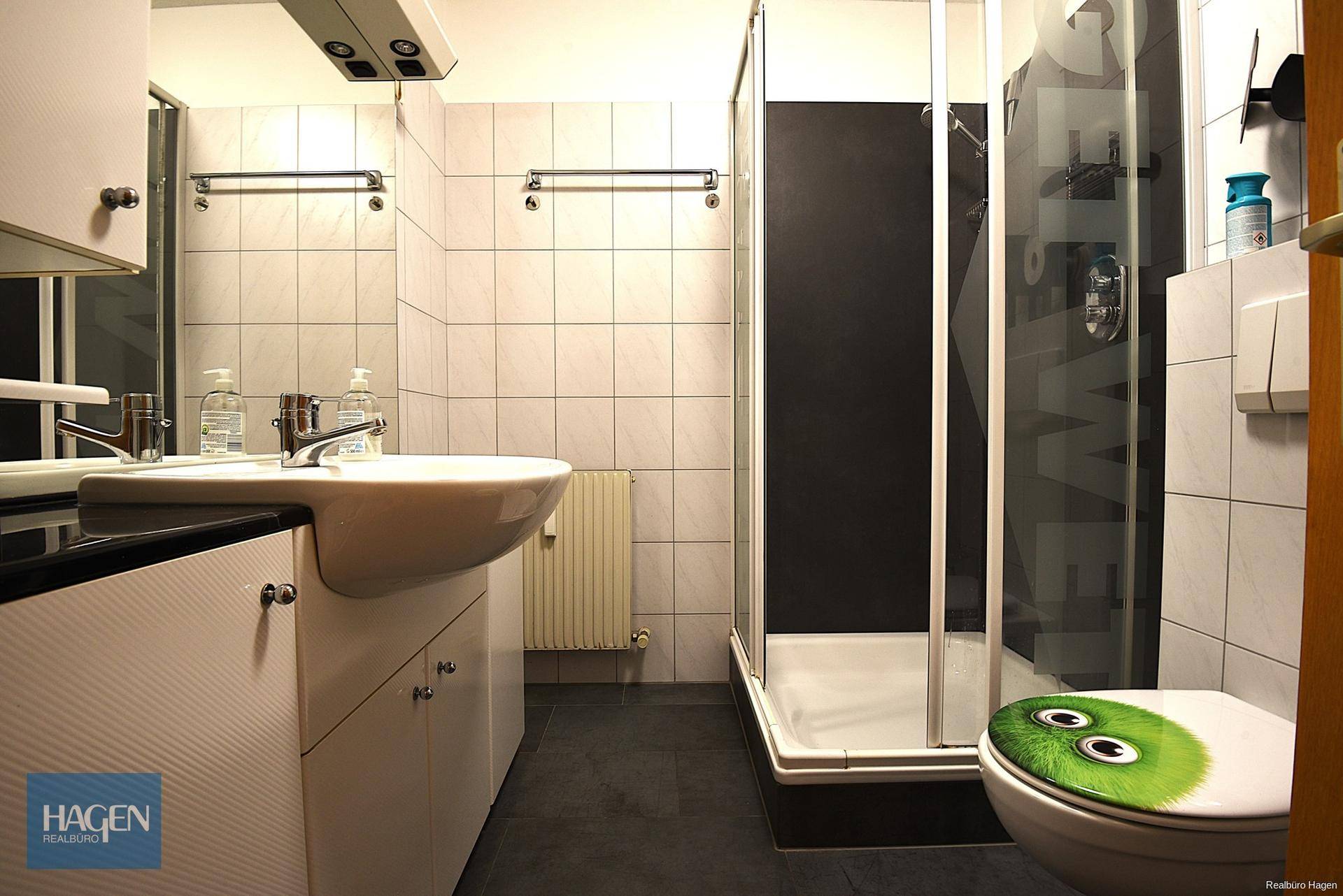 Badezimmer mit Duschkabine, Waschbecken und WC, gefliest in Weiß und Schwarz.