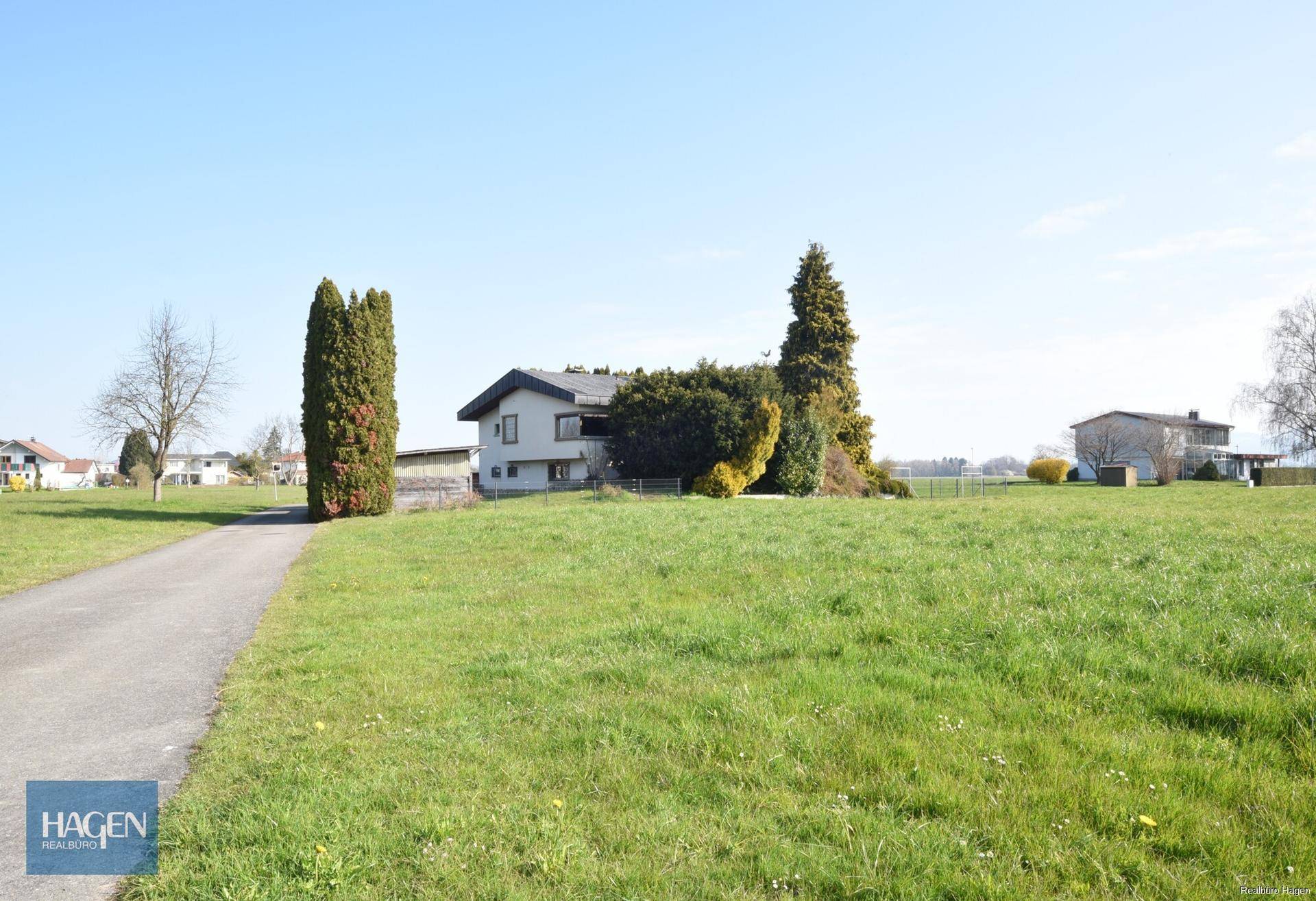 Einfamilienhaus mit weißer Fassade, umgeben von einer weitläufigen grünen Wiese und Bäumen.