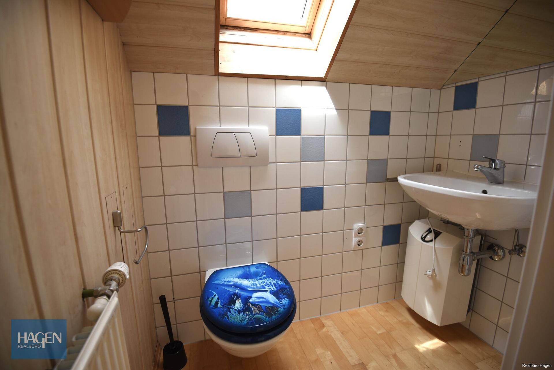 Kleines Badezimmer mit blauen und weißen Fliesen, WC, Waschbecken und Dachfenster.