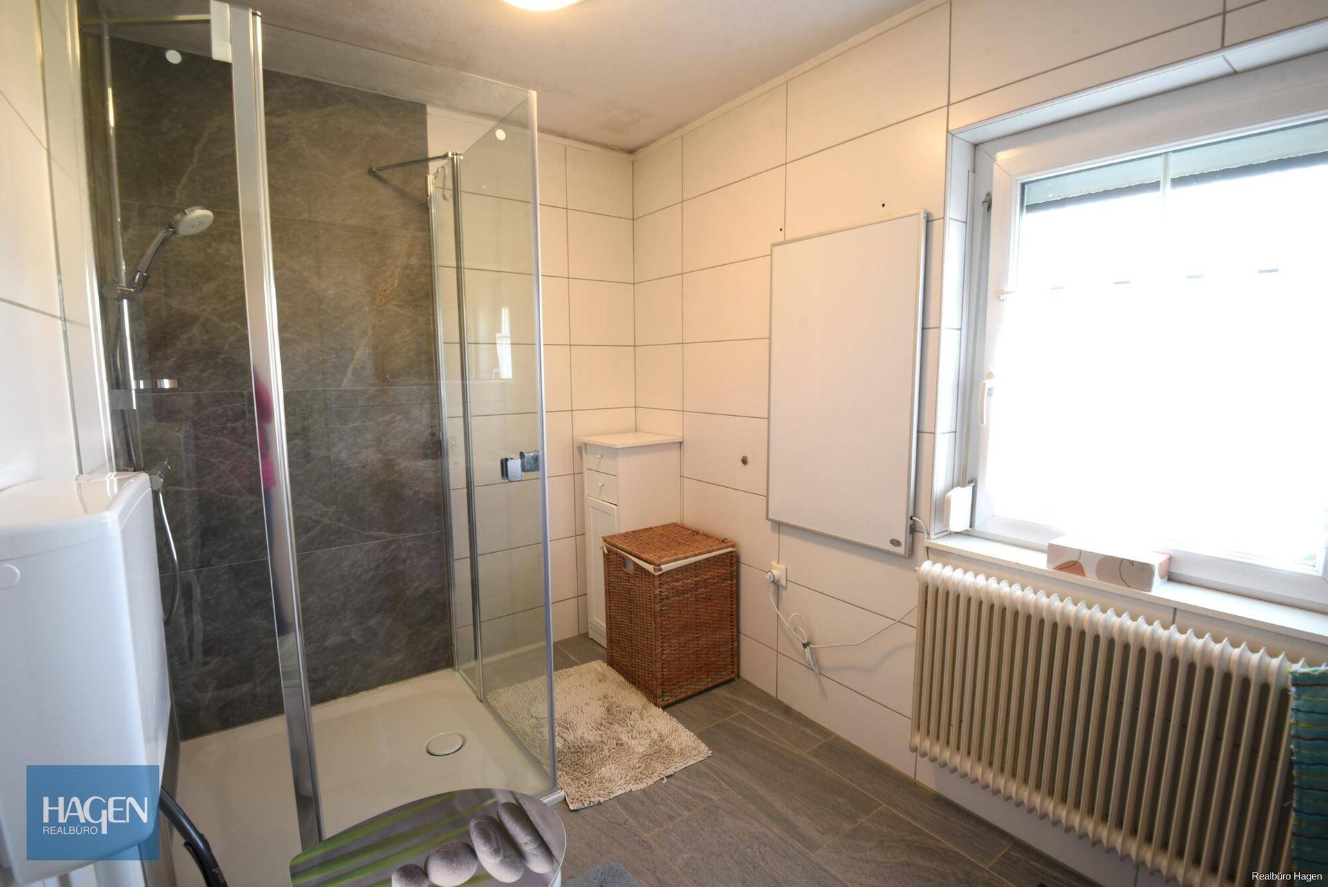 Modernes Badezimmer mit Duschkabine, hellen Fliesen und Fenster für Tageslicht.