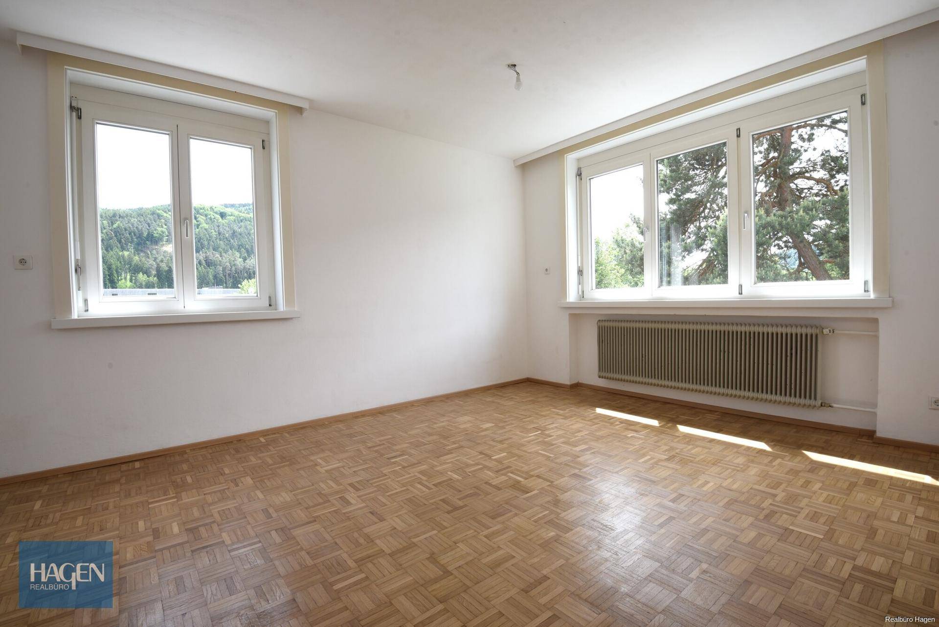 Geräumiges Zimmer mit Parkettboden und großen Fenstern, die einen schönen Blick ins Grüne bieten.