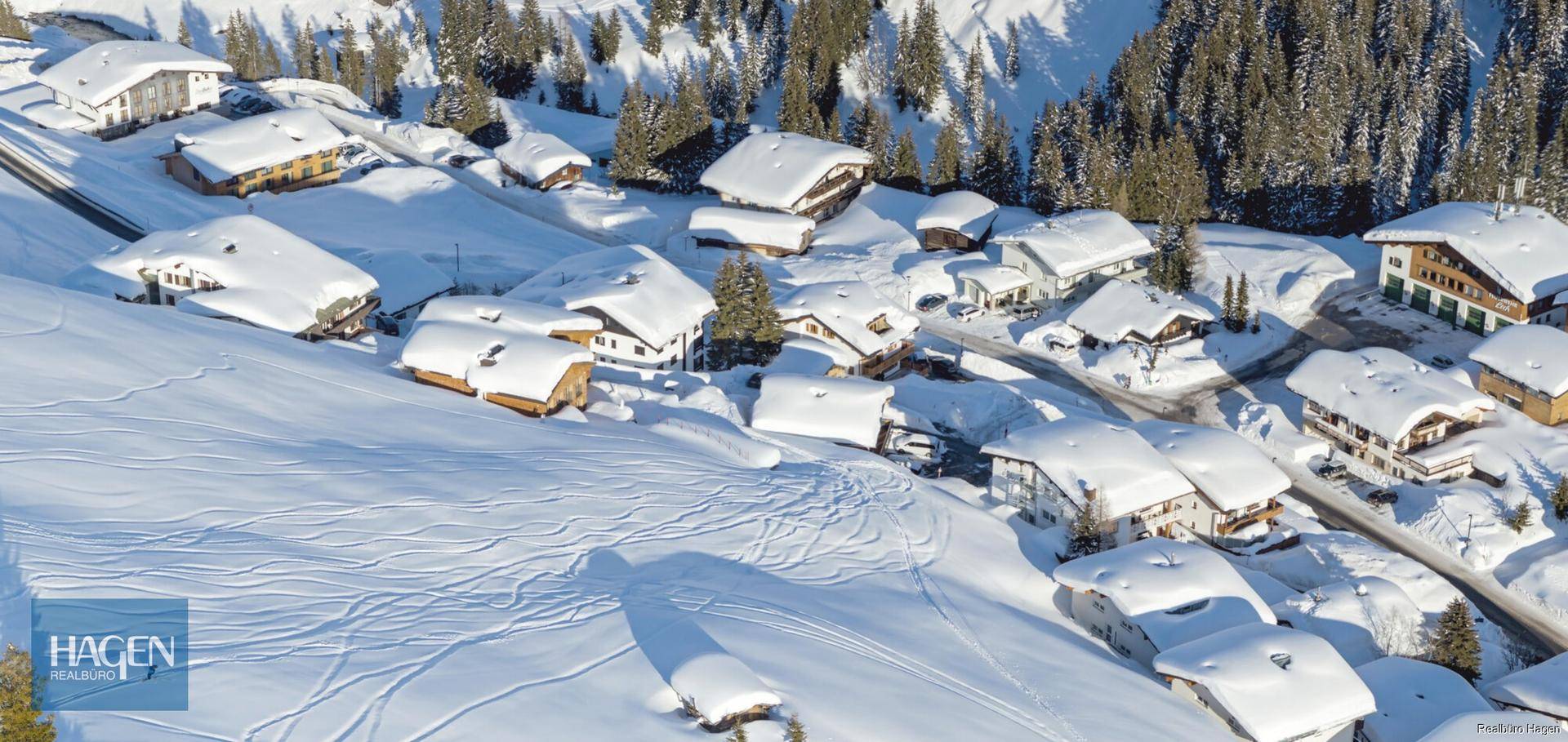 Panoramablick auf ein weitläufiges, schneebedecktes Bergdorf mit vielen traditionellen Häusern.